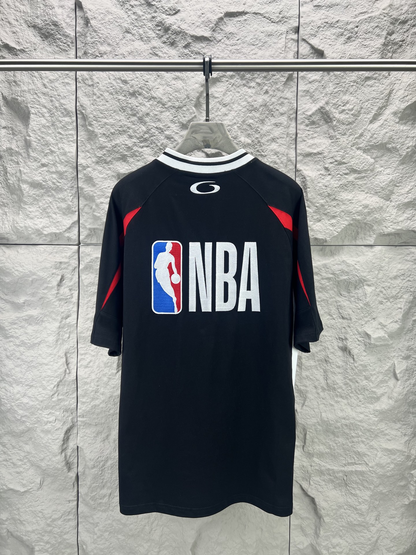 Balenciaga BALENCI*GA × NBA SS26联名T恤 采用科技网眼面料 经透气排汗工艺处理 兼具运动功能性与 廓形 衣身主体为黑色 肩部与袖口拼接撞色饰带 采用精密车缝工艺 线条利落 正面“BALENCIAGA”字样与数字“10”采用立体植绒或贴布绣工艺 边缘锁边牢固 不易脱线 领口为罗纹圆领 采用高弹氨纶混纺材质 久穿不易变形 下摆与袖口采用双针锁边工艺 提升整体耐用性 衣身印有NBA 标识 采用环保胶印工艺 图案清晰牢固 整体设计融合高端时装与运动元素 兼顾舒适穿着与视觉张力 适合潮流穿搭与收藏 整体走线平直细腻 面料舒适柔软 颜色一致无色差 能与同款搭配营造 造型 驾驭各种场合 定制辅料 三标齐全