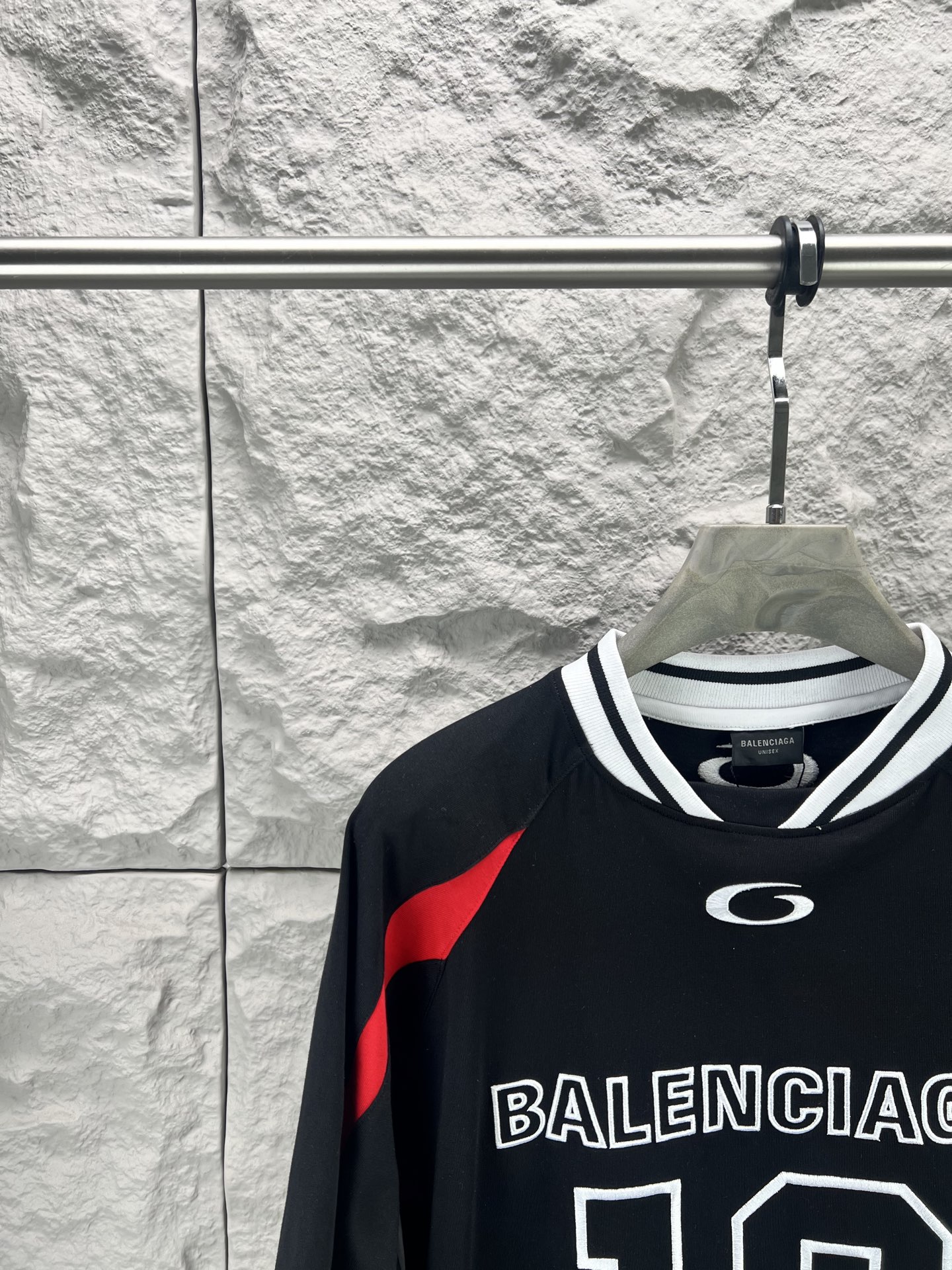 Balenciaga BALENCI*GA × NBA SS26联名T恤 采用科技网眼面料 经透气排汗工艺处理 兼具运动功能性与 廓形 衣身主体为黑色 肩部与袖口拼接撞色饰带 采用精密车缝工艺 线条利落 正面“BALENCIAGA”字样与数字“10”采用立体植绒或贴布绣工艺 边缘锁边牢固 不易脱线 领口为罗纹圆领 采用高弹氨纶混纺材质 久穿不易变形 下摆与袖口采用双针锁边工艺 提升整体耐用性 衣身印有NBA 标识 采用环保胶印工艺 图案清晰牢固 整体设计融合高端时装与运动元素 兼顾舒适穿着与视觉张力 适合潮流穿搭与收藏 整体走线平直细腻 面料舒适柔软 颜色一致无色差 能与同款搭配营造 造型 驾驭各种场合 定制辅料 三标齐全