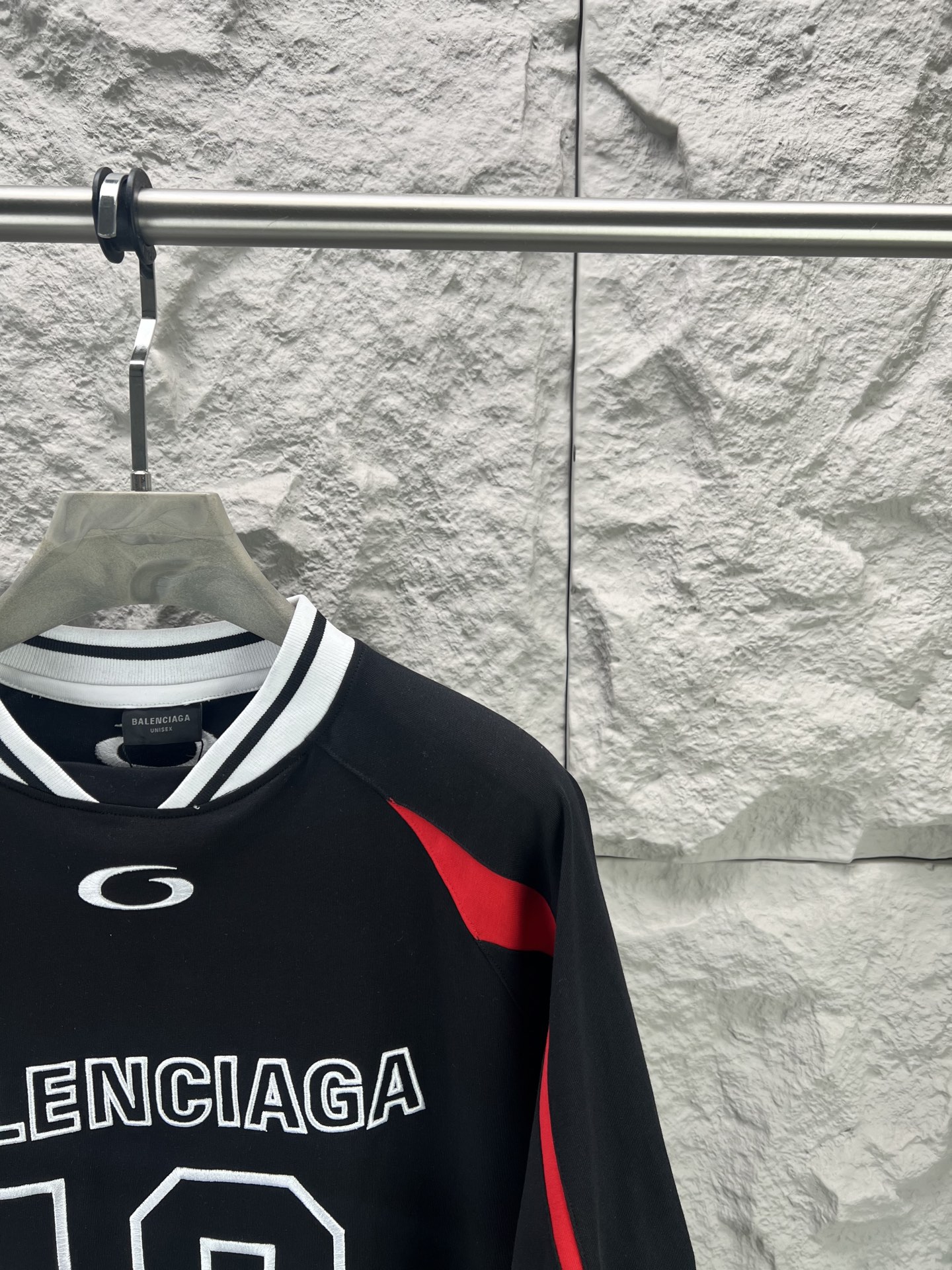 Balenciaga BALENCI*GA × NBA SS26联名T恤 采用科技网眼面料 经透气排汗工艺处理 兼具运动功能性与 廓形 衣身主体为黑色 肩部与袖口拼接撞色饰带 采用精密车缝工艺 线条利落 正面“BALENCIAGA”字样与数字“10”采用立体植绒或贴布绣工艺 边缘锁边牢固 不易脱线 领口为罗纹圆领 采用高弹氨纶混纺材质 久穿不易变形 下摆与袖口采用双针锁边工艺 提升整体耐用性 衣身印有NBA 标识 采用环保胶印工艺 图案清晰牢固 整体设计融合高端时装与运动元素 兼顾舒适穿着与视觉张力 适合潮流穿搭与收藏 整体走线平直细腻 面料舒适柔软 颜色一致无色差 能与同款搭配营造 造型 驾驭各种场合 定制辅料 三标齐全