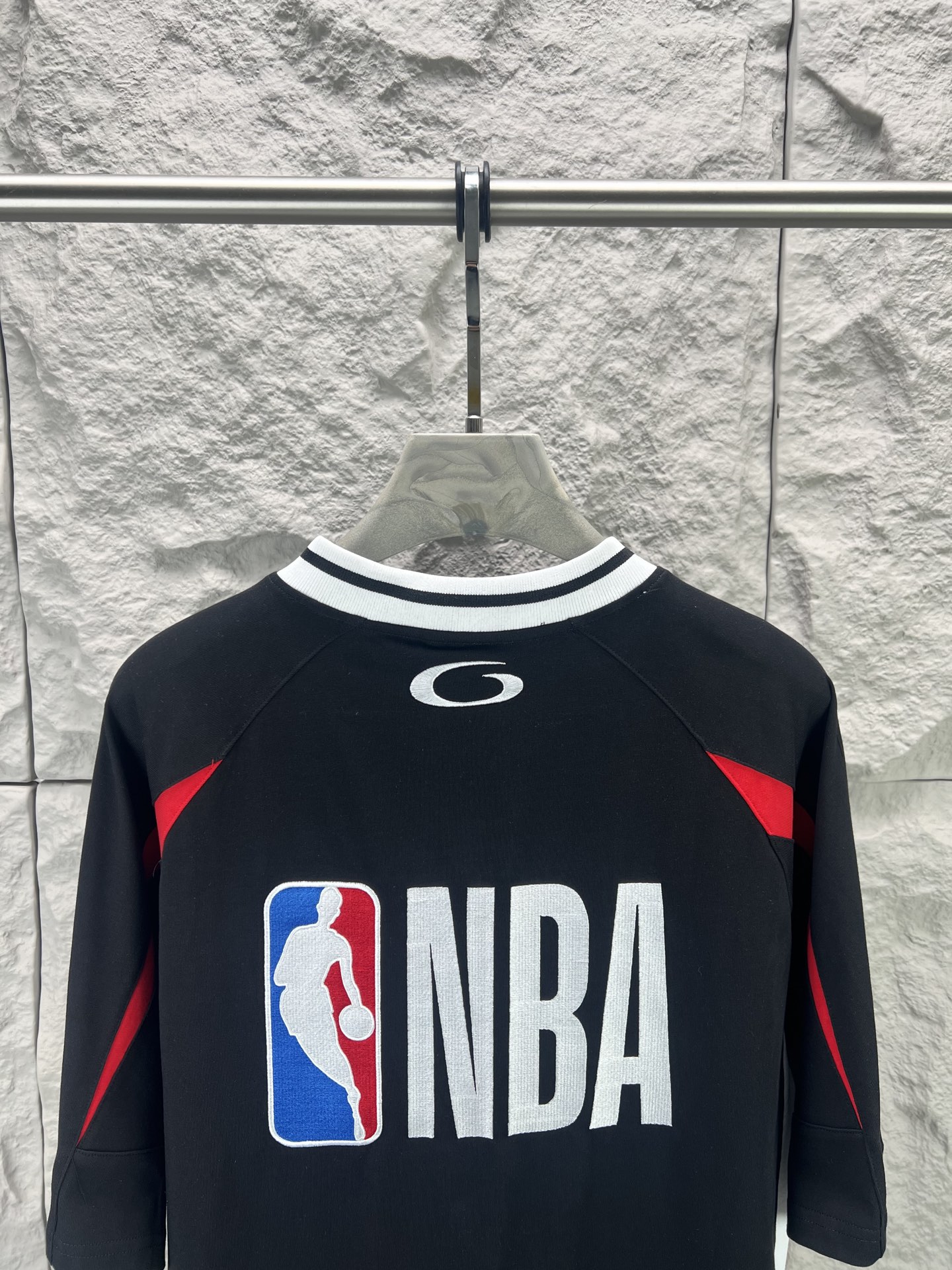 Balenciaga BALENCI*GA × NBA SS26联名T恤 采用科技网眼面料 经透气排汗工艺处理 兼具运动功能性与 廓形 衣身主体为黑色 肩部与袖口拼接撞色饰带 采用精密车缝工艺 线条利落 正面“BALENCIAGA”字样与数字“10”采用立体植绒或贴布绣工艺 边缘锁边牢固 不易脱线 领口为罗纹圆领 采用高弹氨纶混纺材质 久穿不易变形 下摆与袖口采用双针锁边工艺 提升整体耐用性 衣身印有NBA 标识 采用环保胶印工艺 图案清晰牢固 整体设计融合高端时装与运动元素 兼顾舒适穿着与视觉张力 适合潮流穿搭与收藏 整体走线平直细腻 面料舒适柔软 颜色一致无色差 能与同款搭配营造 造型 驾驭各种场合 定制辅料 三标齐全