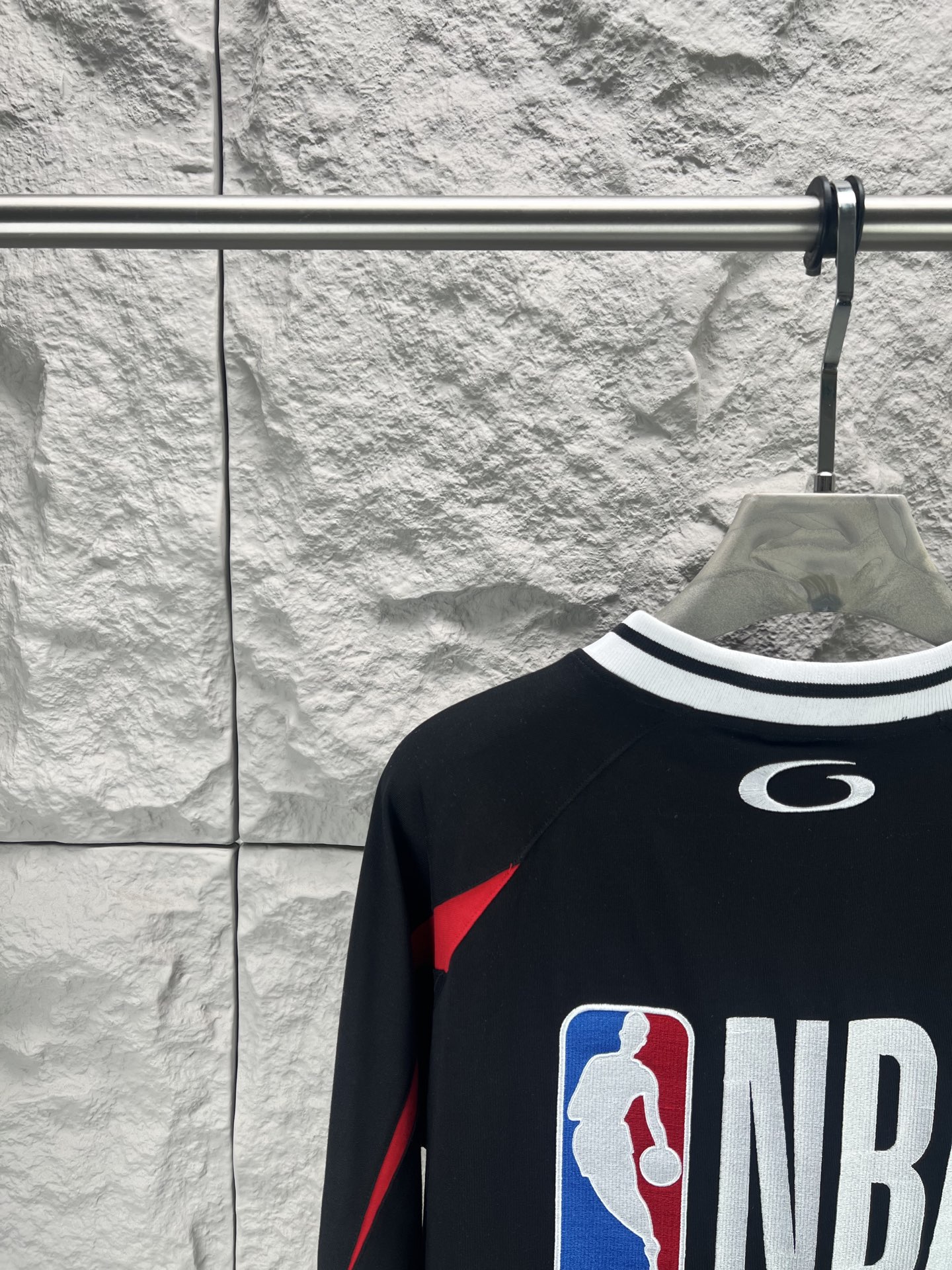 Balenciaga BALENCI*GA × NBA SS26联名T恤 采用科技网眼面料 经透气排汗工艺处理 兼具运动功能性与 廓形 衣身主体为黑色 肩部与袖口拼接撞色饰带 采用精密车缝工艺 线条利落 正面“BALENCIAGA”字样与数字“10”采用立体植绒或贴布绣工艺 边缘锁边牢固 不易脱线 领口为罗纹圆领 采用高弹氨纶混纺材质 久穿不易变形 下摆与袖口采用双针锁边工艺 提升整体耐用性 衣身印有NBA 标识 采用环保胶印工艺 图案清晰牢固 整体设计融合高端时装与运动元素 兼顾舒适穿着与视觉张力 适合潮流穿搭与收藏 整体走线平直细腻 面料舒适柔软 颜色一致无色差 能与同款搭配营造 造型 驾驭各种场合 定制辅料 三标齐全
