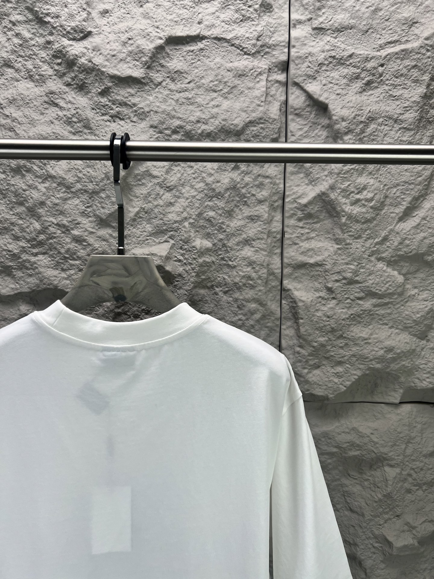 Balenciaga BALENCI*GA 椰树丛林圆领短袖 采用24支特纺紧密棉平纹面料 32支1×1罗纹 面料属于兼具挺括与舒适的中厚型针织 通过紧密纺技术使纤维排列平行 纱体紧致 毛羽显著减少 表面光洁平滑 面料仅经过高温定型机拉幅定形 兼具挺括性与柔软度 垂坠感适中 穿着有型不软塌 领型采用32支罗纹 属于中等偏轻的克重 触感更加柔软轻薄 与中版型的松弛感相呼应 采用渗透印花工艺搭配网点印花制作 渗透印花是一种使染料或浆料深入渗透至纤维内部的印花方式 通过特殊的助剂与压力控制 使色彩沉入面料而非浮于表面 由于采用渗透印花工艺 图案的视觉边界柔和 无胶质感 与白色底布的融合度更高 整体走线平直细腻 面料舒适柔软 颜色一致无色差 能与同款搭配营造 造型 驾驭各种场合 定制辅料 三标齐全