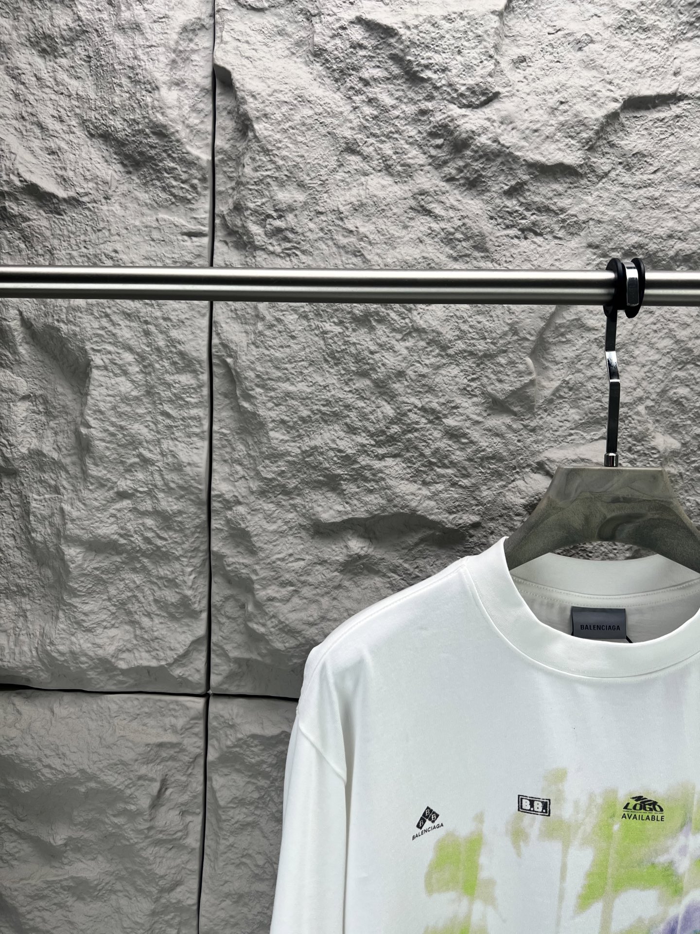 Balenciaga BALENCI*GA 椰树丛林圆领短袖 采用24支特纺紧密棉平纹面料 32支1×1罗纹 面料属于兼具挺括与舒适的中厚型针织 通过紧密纺技术使纤维排列平行 纱体紧致 毛羽显著减少 表面光洁平滑 面料仅经过高温定型机拉幅定形 兼具挺括性与柔软度 垂坠感适中 穿着有型不软塌 领型采用32支罗纹 属于中等偏轻的克重 触感更加柔软轻薄 与中版型的松弛感相呼应 采用渗透印花工艺搭配网点印花制作 渗透印花是一种使染料或浆料深入渗透至纤维内部的印花方式 通过特殊的助剂与压力控制 使色彩沉入面料而非浮于表面 由于采用渗透印花工艺 图案的视觉边界柔和 无胶质感 与白色底布的融合度更高 整体走线平直细腻 面料舒适柔软 颜色一致无色差 能与同款搭配营造 造型 驾驭各种场合 定制辅料 三标齐全