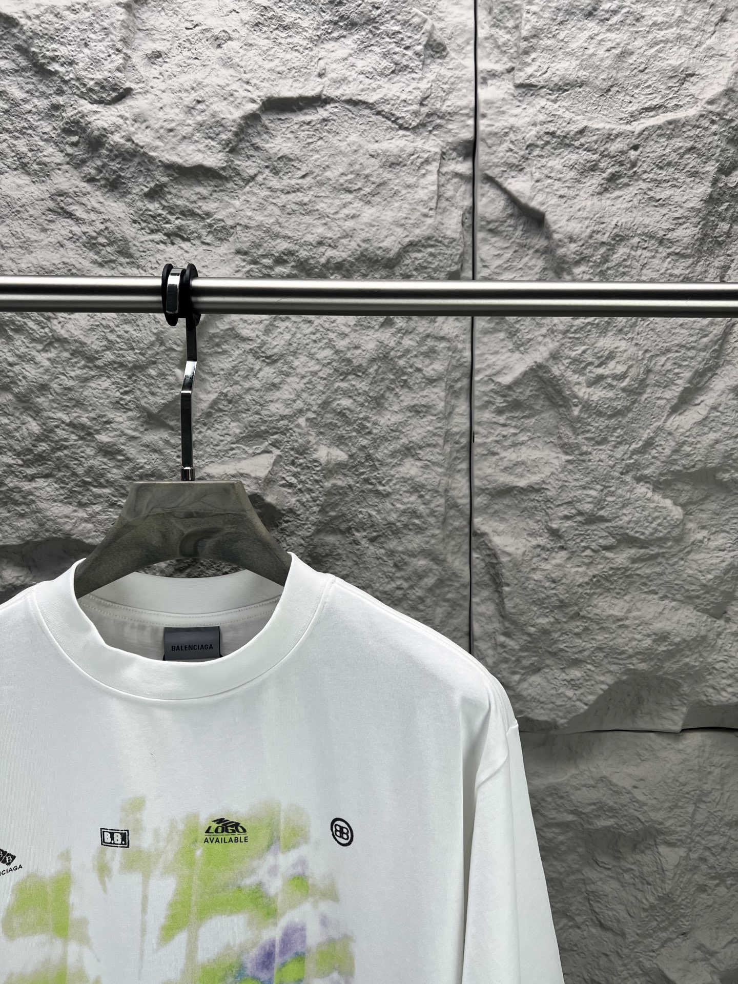 Balenciaga BALENCI*GA 椰树丛林圆领短袖 采用24支特纺紧密棉平纹面料 32支1×1罗纹 面料属于兼具挺括与舒适的中厚型针织 通过紧密纺技术使纤维排列平行 纱体紧致 毛羽显著减少 表面光洁平滑 面料仅经过高温定型机拉幅定形 兼具挺括性与柔软度 垂坠感适中 穿着有型不软塌 领型采用32支罗纹 属于中等偏轻的克重 触感更加柔软轻薄 与中版型的松弛感相呼应 采用渗透印花工艺搭配网点印花制作 渗透印花是一种使染料或浆料深入渗透至纤维内部的印花方式 通过特殊的助剂与压力控制 使色彩沉入面料而非浮于表面 由于采用渗透印花工艺 图案的视觉边界柔和 无胶质感 与白色底布的融合度更高 整体走线平直细腻 面料舒适柔软 颜色一致无色差 能与同款搭配营造 造型 驾驭各种场合 定制辅料 三标齐全