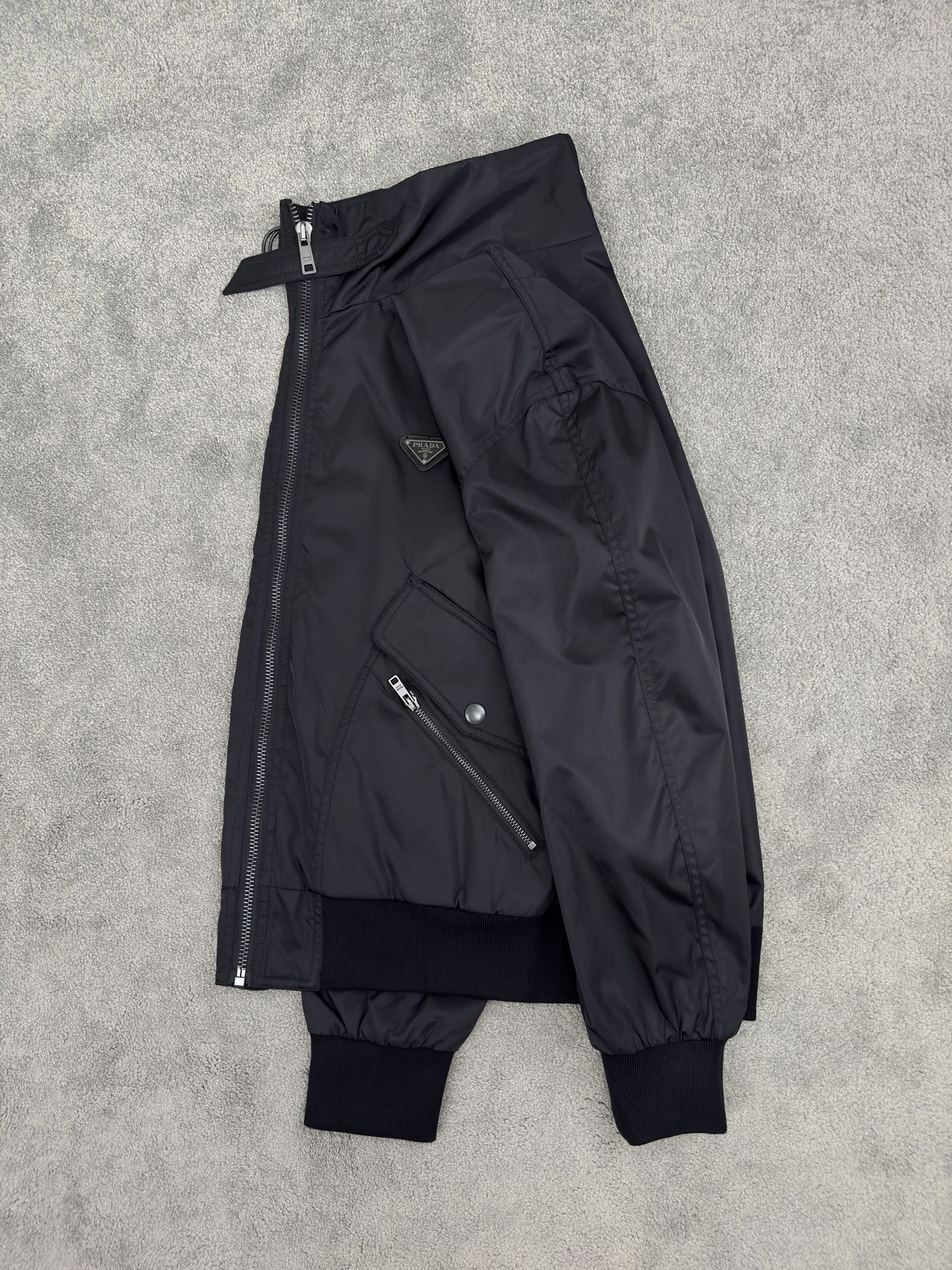 NO:515231,PRADA25 autumn and winter stand collar recycled nylon jacket. It is neatly silhouetted, outlining urban posture, and stand collar design, instantly improving the aura. Large-capacity workwear air pockets are sealed with snap buttons, and are paired with exquisite small bags embellished with zippers. The ribbed cuffs and hem fit the body, and the windproof temperature locks. The enamel triangle metal logo on the chest is painted with enamel, like a cold weapon in the dark night, low-key but highly recognizable. Contrasting orange lining lifts the laces, a blazing orange color appears in front of you, the collision of restraint and ostentatious, and the surprise in details is the exquisite metaphor of PRADA. Color black Size M-3XL (48-56),,prada, jackets & coats,alexander wang19860909PRADA25秋冬立领再生尼龙夹克.利落廓形,勾勒都市姿态,立领设计,瞬间提升气场. 大容量工装风口袋双侧大容量工装风口袋以按扣封缄,搭配拉链点缀的精巧小袋,罗纹袖口&下摆贴合身形,防风锁温. 胸前珐琅三角形金属徽标同色系涂珐处理,如暗夜中的冷兵器,低调却极具辨识度.撞色橙色内衬掀开衣襟,一抹炽烈橙色跃然眼前,内敛与张扬的碰撞,细节处的惊喜,正是PRADA式的精致隐喻. 颜色黑色 尺码M-3XL (48-56),,prada,jackets & coats,alexander wang,Men's clothing