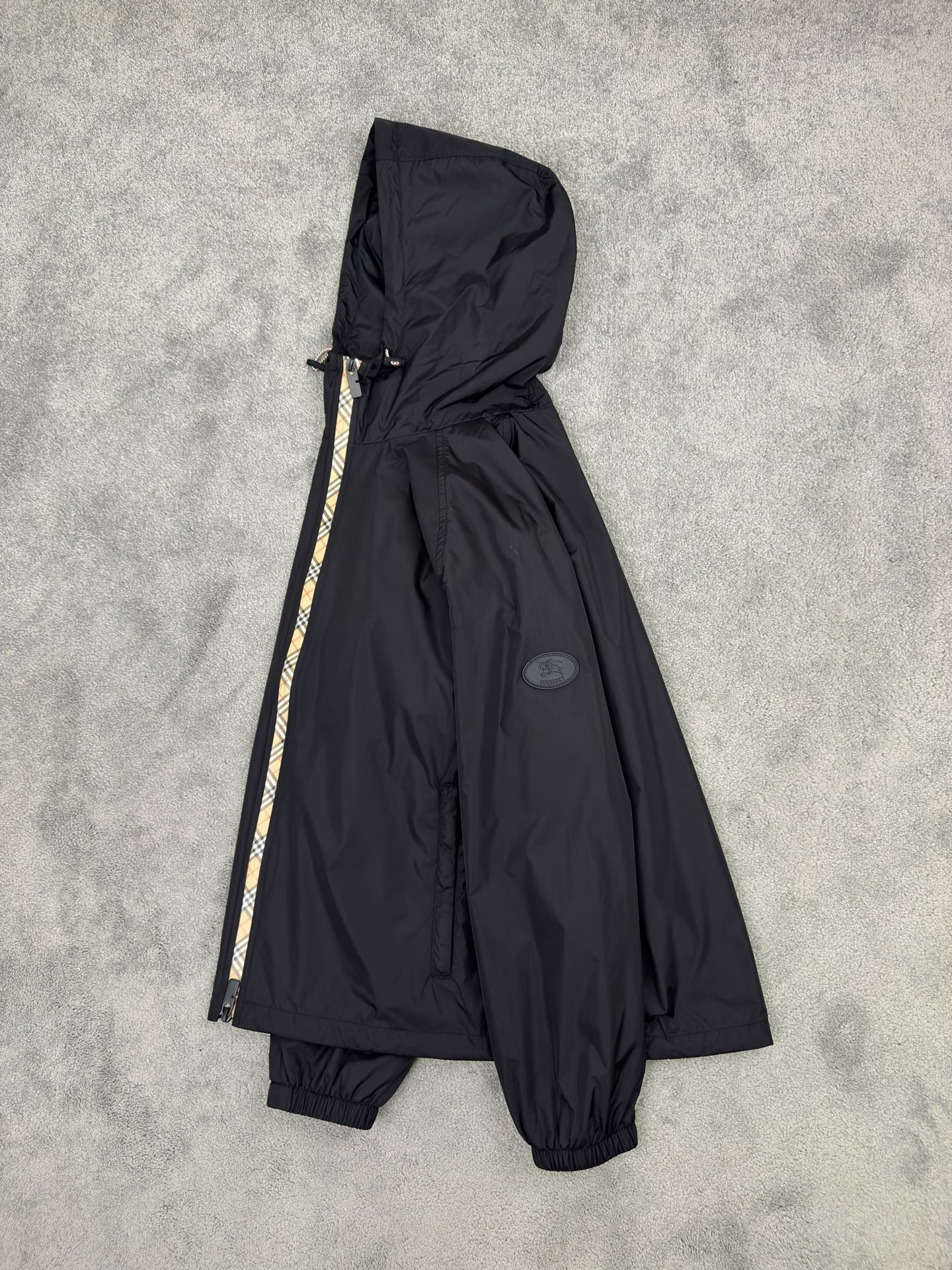 NO:515242,Burberry 25 Autumn and Winter plaid nylon thin cotton hooded jacket. Classic reshaping, agile and windproof. Classic rebirth, plaid contemporary narrative, iconic Burberry plaid wanders around the body in the form of a tape, like a flowing British poem, injecting the elegant genes accumulated by the brand for a century into a modern context. The B-shaped cut zipper head echoes the plaid stitching, and craftsmanship is also seen in the tiny areas. Classic symbols are reborn in innovative craftsmanship. Light nylon fabric, loose silhouette is free and unrestrained. The visual badge of the chivalrous spirit, the equestrian knight pattern on the silicone patch on the chest, originated from the legendary Burberry design of the 1980s. This exquisite decal is not only an index of the brand's history, but also condenses the chivalrous spirit of fearless exploration into visual symbols.  Functional aesthetics, free-waving urban armor, two-way zipper opening and closing smoothly, unlocking different wearing postures. Contrasting color drawstring hood and hem are adjusted with the wind, and windproof is also shaped, adapting to multiple scene needs. The side zipper pockets are hidden and stored to protect the security of personal belongings. The elastic cuffs fit the wrists, neat and not bloated, and make them more free and easy in action. Light nylon fabrics are windproof and waterproof, without fear of changing weather, freely traveling through the city and nature. Ragnarok sleeves, inclusive and diverse postures, and are more relaxed than the regular version, breaking the constraints and giving the body a space for stretching. It does not define your posture, but only fulfills your freedom. Color black Military green Size M-3XL (48-56),,burberry,jackets & coats,hats,alexander wang19860909Burberry25秋冬 格纹饰边尼龙薄棉连帽外套.经典重塑,灵动防风. 经典重生,格纹的当代叙事,标志性 Burberry 格纹以贴带形式游走于衣身,如流动的英伦诗行,将品牌百年积淀的优雅基因注入现代语境.B 型剪裁拉链头与格纹缝线默契呼应,微小之处亦见匠心,经典符号在创新工艺中焕发新生.轻盈尼龙面料,宽松廓形自在不拘束. 骑士精神的视觉徽章,胸前硅胶贴片上的马术骑士图案,源自 1980 年代 Burberry 传奇设计.这枚精致贴花不仅是品牌历史的索引,更将无畏探索的骑士精神凝为视觉符号. 功能美学,自由穿梭的都市铠甲,双向拉链开合流畅启闭,解锁不同穿着姿态.撞色抽绳兜帽与下摆随风调节,防风亦塑形,适配多场景需求.侧边拉链口袋隐蔽收纳,守护随身物品的安全感.弹性袖口贴合手腕,利落不臃肿,行动间更显洒脱.轻盈尼龙面料防风防水,无惧天气变幻,自由穿行城市与自然.插肩袖型,包容多元姿态,比常规版型更松弛的剪裁,打破束缚,赋予身体舒展空间.它不定义你的姿态,只成全你的自在. 颜色黑色 军绿色 尺码M-3XL (48-56),,burberry,jackets & coats,hats,alexander wang,Men's clothing