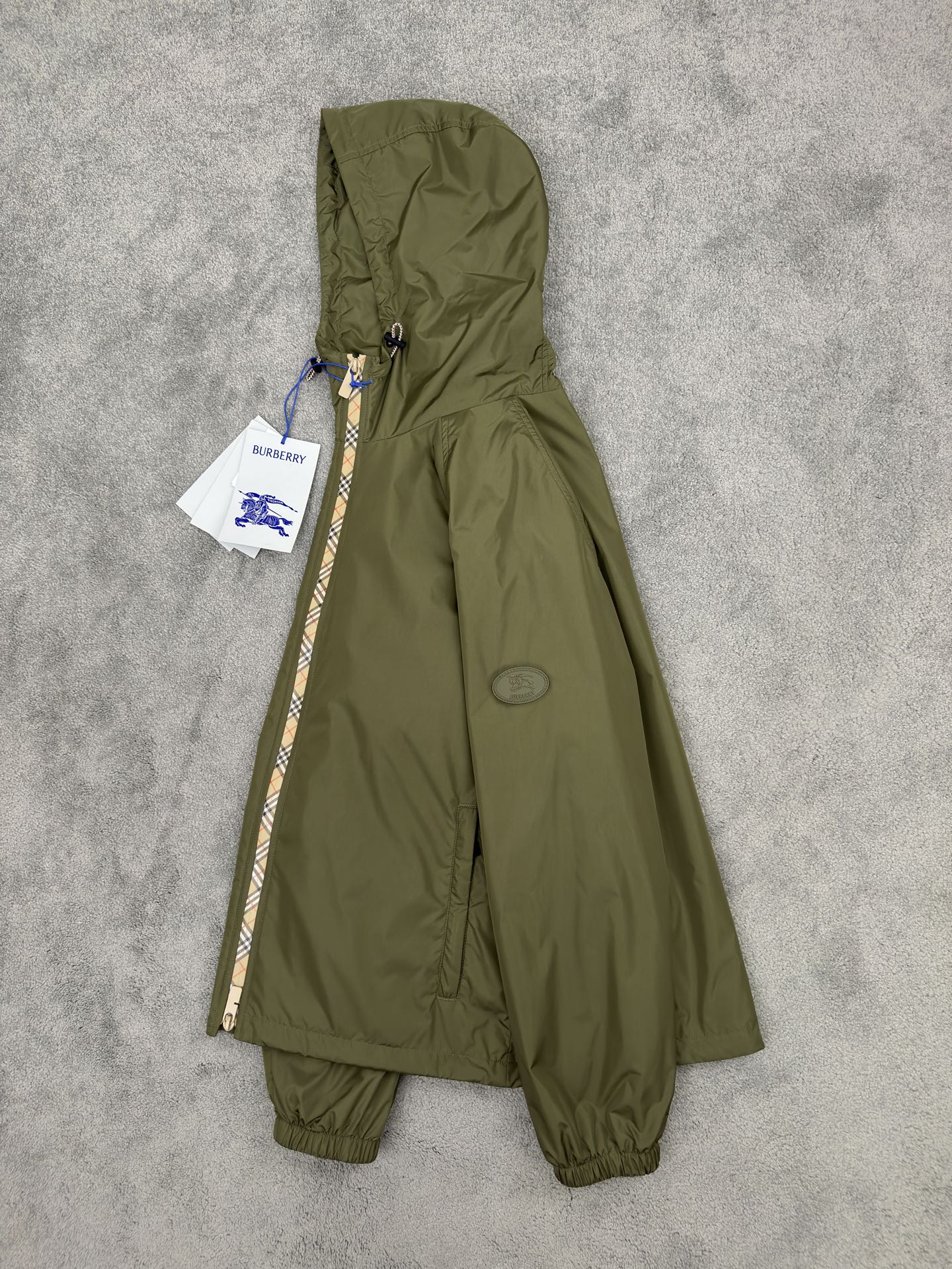 NO:515248,Burberry 25 Autumn and Winter plaid nylon thin cotton hooded jacket. Classic reshaping, agile and windproof. Classic rebirth, plaid contemporary narrative, iconic Burberry plaid wanders around the body in the form of a tape, like a flowing British poem, injecting the elegant genes accumulated by the brand for a century into a modern context. The B-shaped cut zipper head echoes the plaid stitching, and craftsmanship is also seen in the tiny areas. Classic symbols are reborn in innovative craftsmanship. Light nylon fabric, loose silhouette is free and unrestrained. The visual badge of the chivalrous spirit, the equestrian knight pattern on the silicone patch on the chest, originated from the legendary Burberry design of the 1980s. This exquisite decal is not only an index of the brand's history, but also condenses the chivalrous spirit of fearless exploration into visual symbols.  Functional aesthetics, free-waving urban armor, two-way zipper opening and closing smoothly, unlocking different wearing postures. Contrasting color drawstring hood and hem are adjusted with the wind, and windproof is also shaped, adapting to multiple scene needs. The side zipper pockets are hidden and stored to protect the security of personal belongings. The elastic cuffs fit the wrists, neat and not bloated, and make them more free and easy in action. Light nylon fabrics are windproof and waterproof, without fear of changing weather, freely traveling through the city and nature. Ragnarok sleeves, inclusive and diverse postures, and are more relaxed than the regular version, breaking the constraints and giving the body a space for stretching. It does not define your posture, but only fulfills your freedom. Color black Military green Size M-3XL (48-56),,burberry,jackets & coats,hats,alexander wang19860909Burberry25秋冬 格纹饰边尼龙薄棉连帽外套.经典重塑,灵动防风. 经典重生,格纹的当代叙事,标志性 Burberry 格纹以贴带形式游走于衣身,如流动的英伦诗行,将品牌百年积淀的优雅基因注入现代语境.B 型剪裁拉链头与格纹缝线默契呼应,微小之处亦见匠心,经典符号在创新工艺中焕发新生.轻盈尼龙面料,宽松廓形自在不拘束. 骑士精神的视觉徽章,胸前硅胶贴片上的马术骑士图案,源自 1980 年代 Burberry 传奇设计.这枚精致贴花不仅是品牌历史的索引,更将无畏探索的骑士精神凝为视觉符号. 功能美学,自由穿梭的都市铠甲,双向拉链开合流畅启闭,解锁不同穿着姿态.撞色抽绳兜帽与下摆随风调节,防风亦塑形,适配多场景需求.侧边拉链口袋隐蔽收纳,守护随身物品的安全感.弹性袖口贴合手腕,利落不臃肿,行动间更显洒脱.轻盈尼龙面料防风防水,无惧天气变幻,自由穿行城市与自然.插肩袖型,包容多元姿态,比常规版型更松弛的剪裁,打破束缚,赋予身体舒展空间.它不定义你的姿态,只成全你的自在. 颜色黑色 军绿色 尺码M-3XL (48-56),,burberry,jackets & coats,hats,alexander wang,Men's clothing