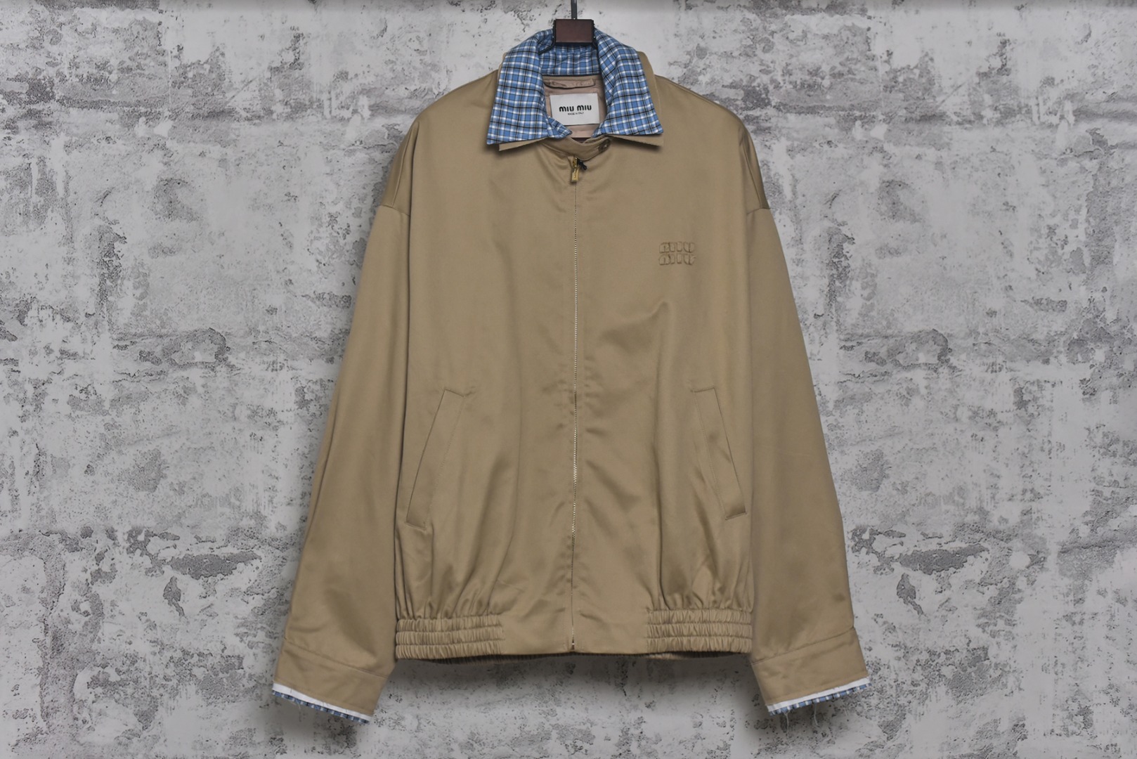 #Miu Miu 25Fw Miu贴布绣格纹假两件夹克外套 定织定染高支数斜纹纺织，赋予面料硬挺的骨骼感与细腻的肌理触感。斜纹结构确保抗皱性与耐久度，同时通过微光泽后整理提升表面质感，呼应现代都市机能美学，选用19姆米级丝绸混纺内衬，以静电覆合技术贴合主体面料，实现无缝一体结构。丝质内里不仅提供亲肤透气性，更通过对比光泽强化内外层次差异，暗藏低调奢华感，复合式拼接设计，领口、袖口采用蓝格纹拼接设计，通过激光裁切包边工艺实现精准对格。拼接部位以隐藏式埋夹缝制衔接，边缘做0.3cm仿旧毛边处理，模拟自然磨损的复古效果，同时与主面料形成粗犷与精致的材质对话，定制镀金色五金拉链，选用日本YKK EXCELL系列底链，齿牙经PVD真空镀金处理，达到3级耐磨标准。拉头内部嵌入硅胶减震垫片，实现静音开合，表面做做旧蚀刻工艺呈现斑驳肌理，避免工业感过强，每颗纽扣取材于水牛角切片，经手工抛光保留天然纹理与半透光特性缠绕同色系绣线防止脱落，细节体现传统工艺与现代设计的融合 尺码：S-L【不拉拉链可以不用考虑体重】-选品中心