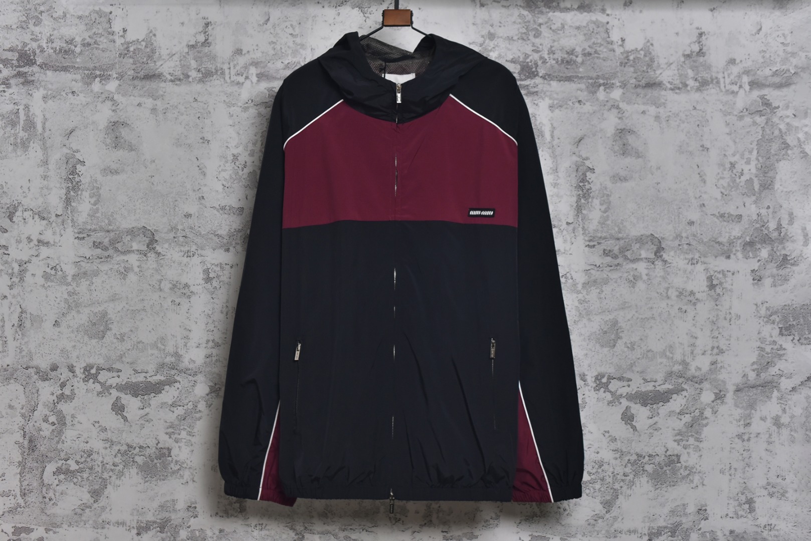 #Miu Miu 25Fw Miu小标拼色玫红连帽外套 梭织拼色主体，高密尼龙塔丝隆，采用30D/72超细旦纱线，经平纹+斜纹复合织造，表面做耐久防泼水涂层处理，可日常生活防水，激光切割拼缝，色块接缝处采用0.1mm级精密切割以热风压胶条，内衬加固。定制弹力捆条选用210T涤纶四面弹，经预缩处理后以45°斜裁包边，边缘采用三针五线收口，确保拉伸不变形，定织提花织带，以32股高强涤纶长丝织造，表面呈现MIUMIU专属提花Logo，通过纱罗组织实现透气镂空。米色动态调节抽绳，双通道抽绳管，可单手调节。绳扣内部设微型棘齿结构，防止运动中松动，采用立体冲孔网布，以5mm厚度+70%开孔率的聚酯单丝编织，背部复合吸湿速干氨纶，定制合金拉链，链齿采用亮光氧化锆陶瓷，拉头内嵌双轴承滑轮，顺滑度达20,000次测试无卡顿 尺码：44 46 48-选品中心