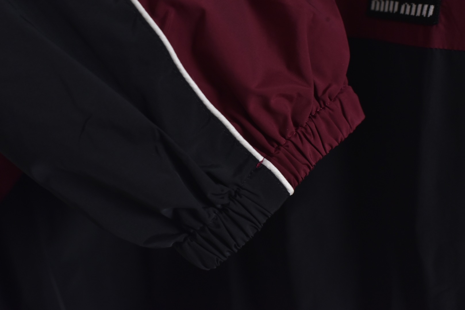 图片[6]-#Miu Miu 25Fw Miu小标拼色玫红连帽外套 梭织拼色主体，高密尼龙塔丝隆，采用30D/72超细旦纱线，经平纹+斜纹复合织造，表面做耐久防泼水涂层处理，可日常生活防水，激光切割拼缝，色块接缝处采用0.1mm级精密切割以热风压胶条，内衬加固。定制弹力捆条选用210T涤纶四面弹，经预缩处理后以45°斜裁包边，边缘采用三针五线收口，确保拉伸不变形，定织提花织带，以32股高强涤纶长丝织造，表面呈现MIUMIU专属提花Logo，通过纱罗组织实现透气镂空。米色动态调节抽绳，双通道抽绳管，可单手调节。绳扣内部设微型棘齿结构，防止运动中松动，采用立体冲孔网布，以5mm厚度+70%开孔率的聚酯单丝编织，背部复合吸湿速干氨纶，定制合金拉链，链齿采用亮光氧化锆陶瓷，拉头内嵌双轴承滑轮，顺滑度达20,000次测试无卡顿 尺码：44 46 48-选品中心