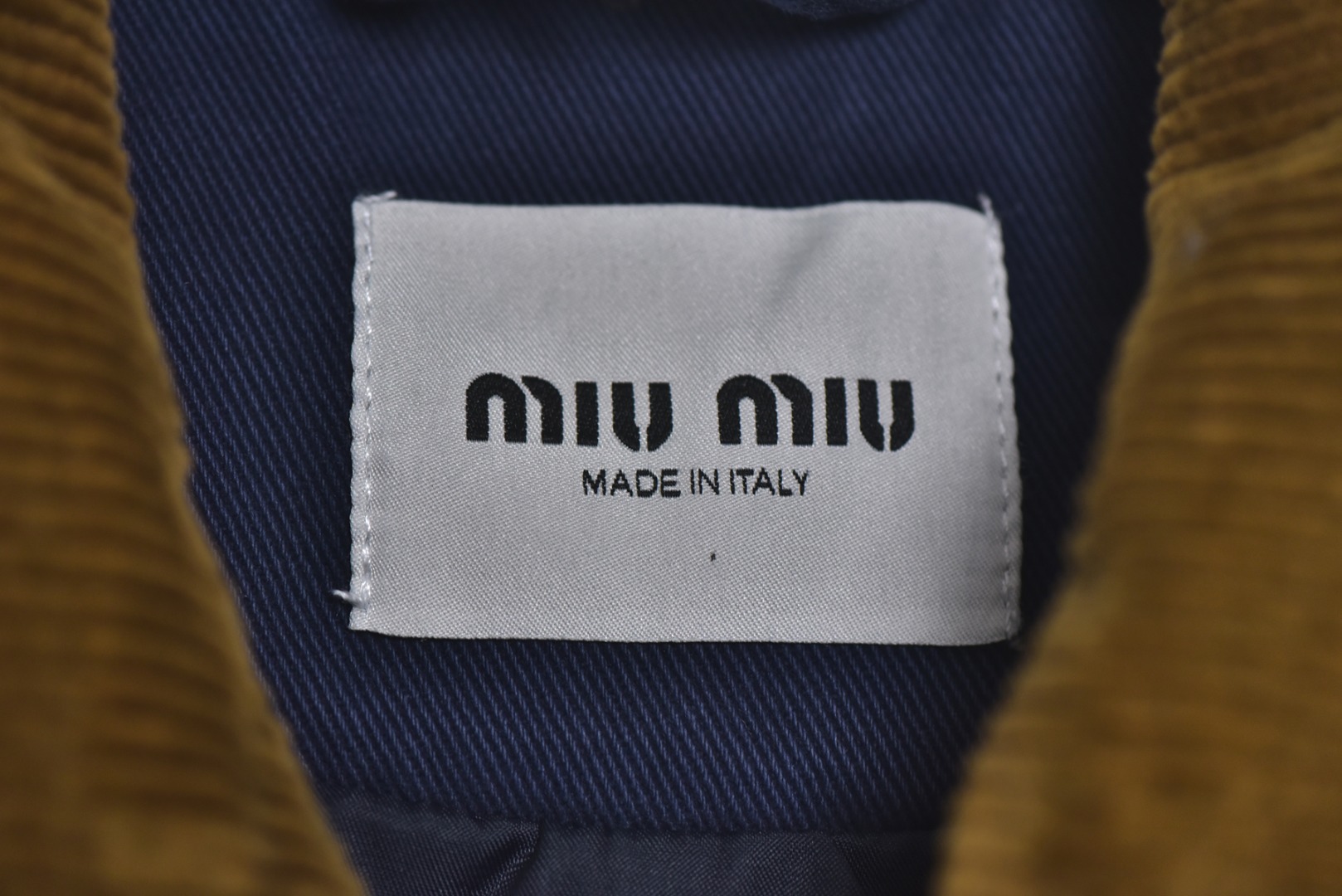 图片[4]-#Miu Miu 25Fw Miu小标法工夹棉外套 采用16OZ进口高克重牛仔面料，选用更长绒的优质棉花纺成高捻度的特规纱线，以确保最终面料的强度与最终染色的纯净度。经典的牛仔斜纹织法被精确校准，以在达成高密度的同时，保留恰到好处的柔软潜力，避免过于板硬。经纬纱的排列密度远超普通牛仔，从而获得极高的抗撕裂强度和耐磨性。定染对版色纺法工蓝，染色工程师需要反复调试靛蓝的配方，精确控制染色温度、时长和氧化次数，通过多层重复染色来模拟出时间赋予的色彩层次感。内里填充400D洗水棉，填充物为经过预洗处理的棉絮。“预洗水”工艺至关重要，它去除了棉絮的“新”感和僵硬感，使其从一开始就呈现出柔软、蓬松且略带旧化肌理的触感，确保外套穿着时立即舒适，且外观呈现出自然的蓬松感和慵懒的廓形。领部材质选用特规灯芯绒，其绒条宽度和棉绒品质均为定制，以匹配主面料的厚重质感与复古风格。胸前贴布绣花首先将设计好的图案以定制裁片的形式制作出来，再以精密缝纫的方式固定在胸前主体上。这款法工外套，是一件融合了传统工装基因与高级时装工艺的复杂作品。从独家定织定染的面料，到创新性的400D洗水棉填充结构，再到耗时费工的拼接领部与立体贴布绣花，每一个环节都设置了极高的技术和成本门槛。它不仅仅是一件外套，更是一件体现了品牌对材料学、工艺学和美学极致追求的“可穿戴艺术品”。 尺码：38 40 42-选品中心