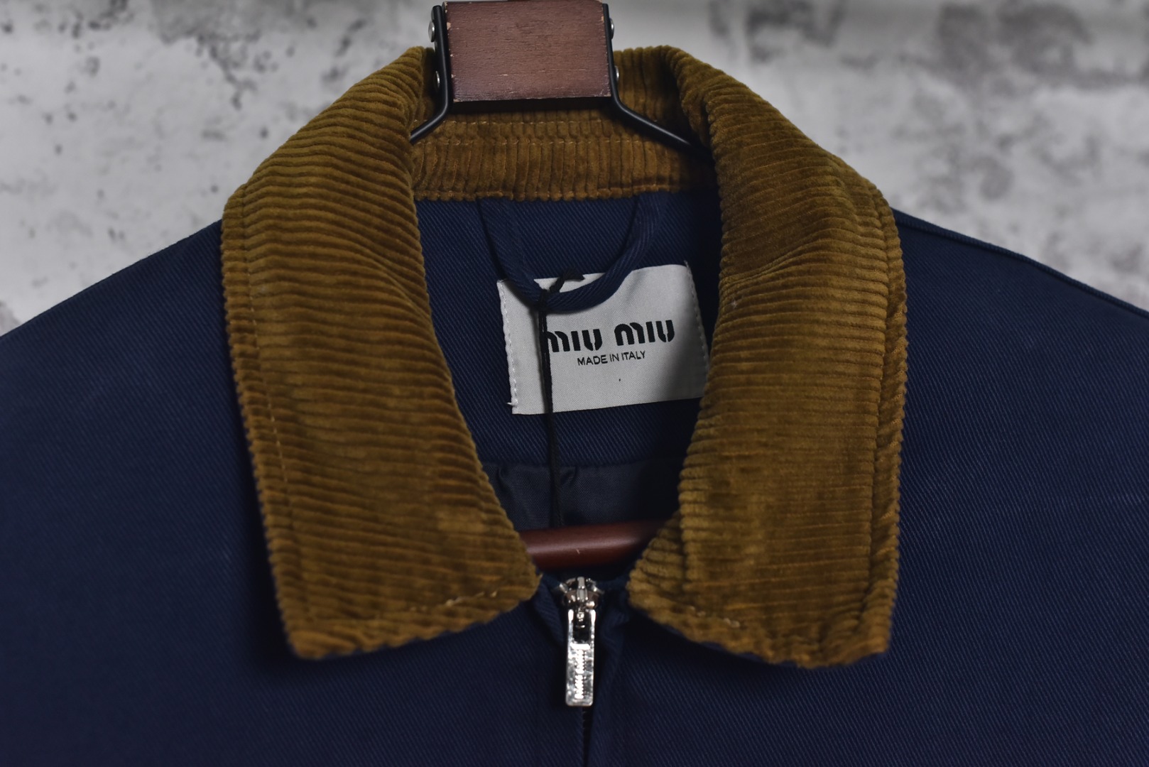 图片[6]-#Miu Miu 25Fw Miu小标法工夹棉外套 采用16OZ进口高克重牛仔面料，选用更长绒的优质棉花纺成高捻度的特规纱线，以确保最终面料的强度与最终染色的纯净度。经典的牛仔斜纹织法被精确校准，以在达成高密度的同时，保留恰到好处的柔软潜力，避免过于板硬。经纬纱的排列密度远超普通牛仔，从而获得极高的抗撕裂强度和耐磨性。定染对版色纺法工蓝，染色工程师需要反复调试靛蓝的配方，精确控制染色温度、时长和氧化次数，通过多层重复染色来模拟出时间赋予的色彩层次感。内里填充400D洗水棉，填充物为经过预洗处理的棉絮。“预洗水”工艺至关重要，它去除了棉絮的“新”感和僵硬感，使其从一开始就呈现出柔软、蓬松且略带旧化肌理的触感，确保外套穿着时立即舒适，且外观呈现出自然的蓬松感和慵懒的廓形。领部材质选用特规灯芯绒，其绒条宽度和棉绒品质均为定制，以匹配主面料的厚重质感与复古风格。胸前贴布绣花首先将设计好的图案以定制裁片的形式制作出来，再以精密缝纫的方式固定在胸前主体上。这款法工外套，是一件融合了传统工装基因与高级时装工艺的复杂作品。从独家定织定染的面料，到创新性的400D洗水棉填充结构，再到耗时费工的拼接领部与立体贴布绣花，每一个环节都设置了极高的技术和成本门槛。它不仅仅是一件外套，更是一件体现了品牌对材料学、工艺学和美学极致追求的“可穿戴艺术品”。 尺码：38 40 42-选品中心