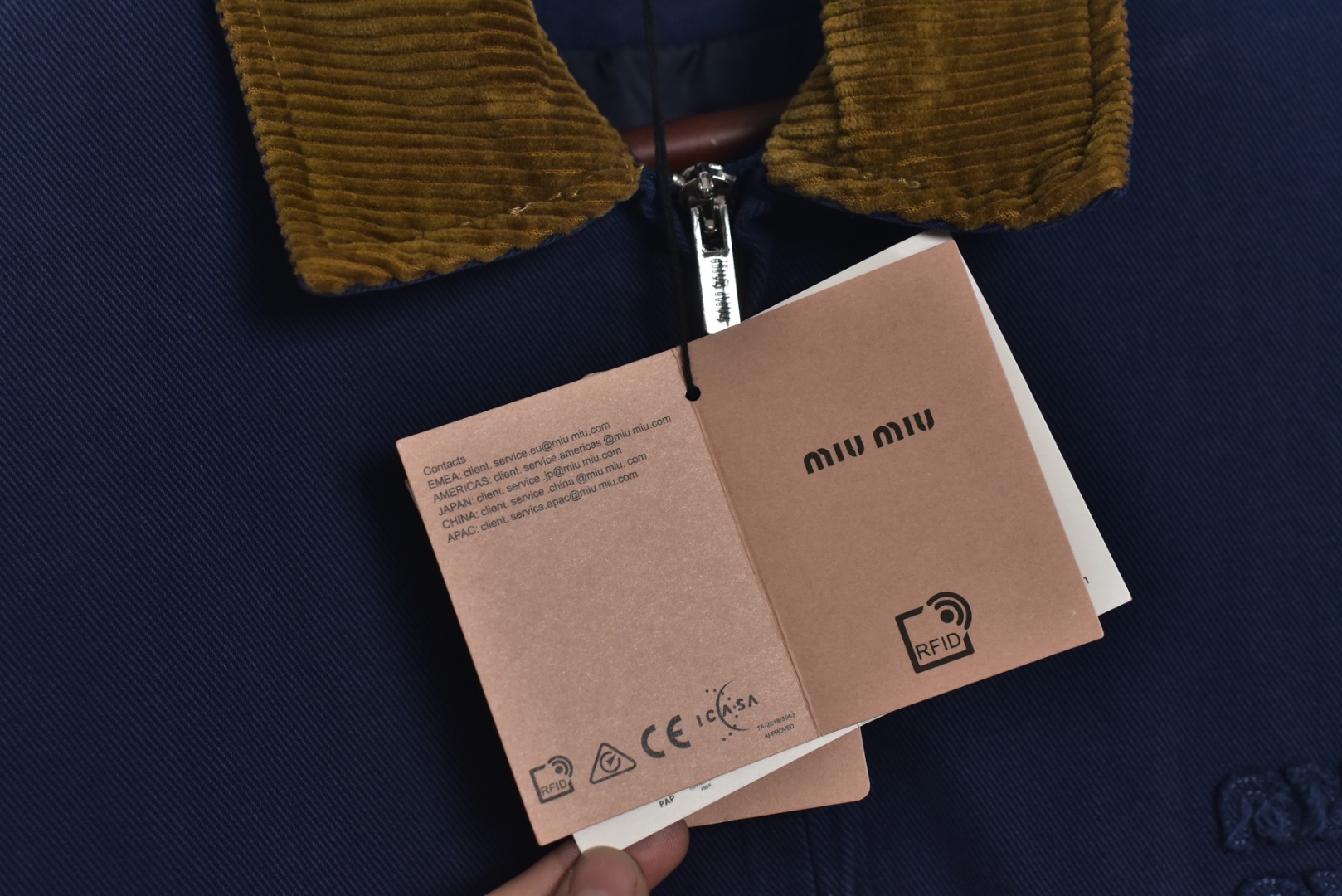 图片[7]-#Miu Miu 25Fw Miu小标法工夹棉外套 采用16OZ进口高克重牛仔面料，选用更长绒的优质棉花纺成高捻度的特规纱线，以确保最终面料的强度与最终染色的纯净度。经典的牛仔斜纹织法被精确校准，以在达成高密度的同时，保留恰到好处的柔软潜力，避免过于板硬。经纬纱的排列密度远超普通牛仔，从而获得极高的抗撕裂强度和耐磨性。定染对版色纺法工蓝，染色工程师需要反复调试靛蓝的配方，精确控制染色温度、时长和氧化次数，通过多层重复染色来模拟出时间赋予的色彩层次感。内里填充400D洗水棉，填充物为经过预洗处理的棉絮。“预洗水”工艺至关重要，它去除了棉絮的“新”感和僵硬感，使其从一开始就呈现出柔软、蓬松且略带旧化肌理的触感，确保外套穿着时立即舒适，且外观呈现出自然的蓬松感和慵懒的廓形。领部材质选用特规灯芯绒，其绒条宽度和棉绒品质均为定制，以匹配主面料的厚重质感与复古风格。胸前贴布绣花首先将设计好的图案以定制裁片的形式制作出来，再以精密缝纫的方式固定在胸前主体上。这款法工外套，是一件融合了传统工装基因与高级时装工艺的复杂作品。从独家定织定染的面料，到创新性的400D洗水棉填充结构，再到耗时费工的拼接领部与立体贴布绣花，每一个环节都设置了极高的技术和成本门槛。它不仅仅是一件外套，更是一件体现了品牌对材料学、工艺学和美学极致追求的“可穿戴艺术品”。 尺码：38 40 42-选品中心