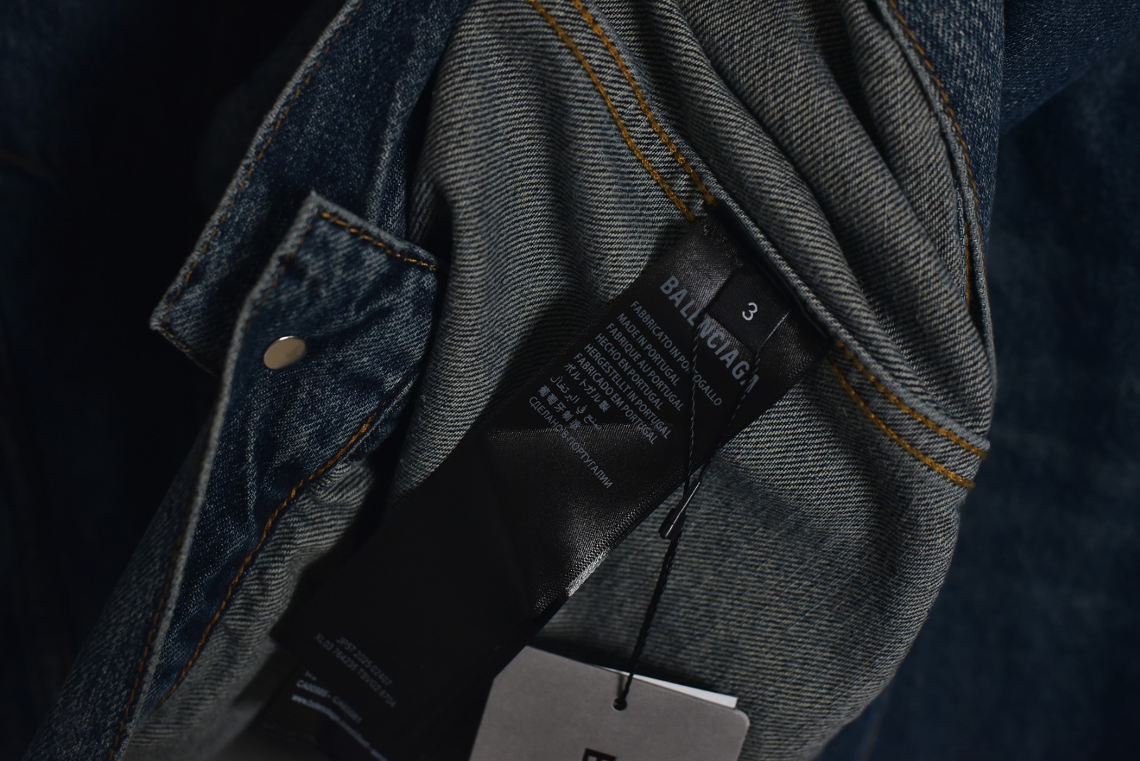 图片[9]-#Balenciaga/巴黎世家 25Fw 银胶带印花蓝牛仔外套 定制赛络纺工艺牛仔面料。此工艺使两根粗纱在纺纱阶段保持一定间距，经牵伸后由前罗拉输出，再汇合加捻成一根单纱。 赛络纺技术使最终织造出的丹宁面料具有卓越的强度、优异的耐磨性以及独特的柔软手感。纱线结构紧密，面料纹理清晰、光泽柔和，布面毛羽显著减少，呈现出普通牛仔无法比拟的细腻、挺括且高质感的视觉和触觉体验，为后续的重工艺处理提供了完美的基础。所有接缝、拼接处均采用高张力、高密度、均匀一致的针距进行缝制。线迹精准如机械制图，无任何跳针、断线或线头。内侧包边处理工整，承受高强度穿着与洗涤后仍能保持结构稳定，体现了世界级大厂对生产流程的严苛品控和无可挑剔的缝制技术。印花工艺复杂性： 这是整件外套最具技术挑战性的部分，其“胶带”效果并非普通印花或贴膜，而是采用了极为繁琐的多层厚板胶浆印花与特种闪粉混合印刷技术。厚板印刷： 通过多次重复印刷特调高分子胶浆，在面料表面堆叠出具有显著3D立体浮雕感的“胶带”条纹。每一次印刷都需经过精确对位和高温烘干定型，确保图案边缘锐利如刀刻，厚度均匀一致，手感坚硬且极具冲击力。闪粉融合： 在胶浆未完全固化前，将定制的高折射率微闪片通过精密筛网均匀撒在印花表面，并使其牢固嵌入胶浆内部。此步骤需精确控制胶浆粘度和闪粉的附着力，确保闪粉分布均匀、牢固不脱落，且光泽璀璨持久。 品质体现： 最终形成的印花图案不仅具有强烈的视觉立体感和触摸感，更因其高强度的物化特性，实现了极高的耐撕裂性、抗皱性和耐洗牢度。印花部分不会开裂、剥落或变黄，闪粉在日常穿着中也能最大限度地保持其闪耀效果，经久如新。这种工艺将装饰性与功能性推向了极致，成本高昂，良品率极低，是大厂才能驾驭的复杂技术 尺码：1 2 3-选品中心