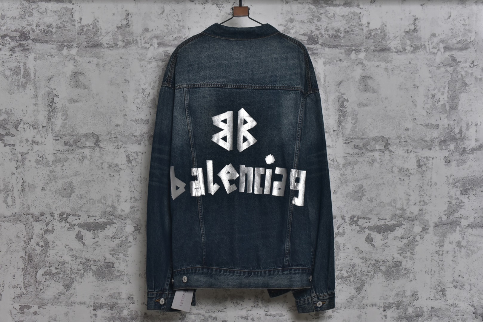 图片[2]-#Balenciaga/巴黎世家 25Fw 银胶带印花蓝牛仔外套 定制赛络纺工艺牛仔面料。此工艺使两根粗纱在纺纱阶段保持一定间距，经牵伸后由前罗拉输出，再汇合加捻成一根单纱。 赛络纺技术使最终织造出的丹宁面料具有卓越的强度、优异的耐磨性以及独特的柔软手感。纱线结构紧密，面料纹理清晰、光泽柔和，布面毛羽显著减少，呈现出普通牛仔无法比拟的细腻、挺括且高质感的视觉和触觉体验，为后续的重工艺处理提供了完美的基础。所有接缝、拼接处均采用高张力、高密度、均匀一致的针距进行缝制。线迹精准如机械制图，无任何跳针、断线或线头。内侧包边处理工整，承受高强度穿着与洗涤后仍能保持结构稳定，体现了世界级大厂对生产流程的严苛品控和无可挑剔的缝制技术。印花工艺复杂性： 这是整件外套最具技术挑战性的部分，其“胶带”效果并非普通印花或贴膜，而是采用了极为繁琐的多层厚板胶浆印花与特种闪粉混合印刷技术。厚板印刷： 通过多次重复印刷特调高分子胶浆，在面料表面堆叠出具有显著3D立体浮雕感的“胶带”条纹。每一次印刷都需经过精确对位和高温烘干定型，确保图案边缘锐利如刀刻，厚度均匀一致，手感坚硬且极具冲击力。闪粉融合： 在胶浆未完全固化前，将定制的高折射率微闪片通过精密筛网均匀撒在印花表面，并使其牢固嵌入胶浆内部。此步骤需精确控制胶浆粘度和闪粉的附着力，确保闪粉分布均匀、牢固不脱落，且光泽璀璨持久。 品质体现： 最终形成的印花图案不仅具有强烈的视觉立体感和触摸感，更因其高强度的物化特性，实现了极高的耐撕裂性、抗皱性和耐洗牢度。印花部分不会开裂、剥落或变黄，闪粉在日常穿着中也能最大限度地保持其闪耀效果，经久如新。这种工艺将装饰性与功能性推向了极致，成本高昂，良品率极低，是大厂才能驾驭的复杂技术 尺码：1 2 3-选品中心