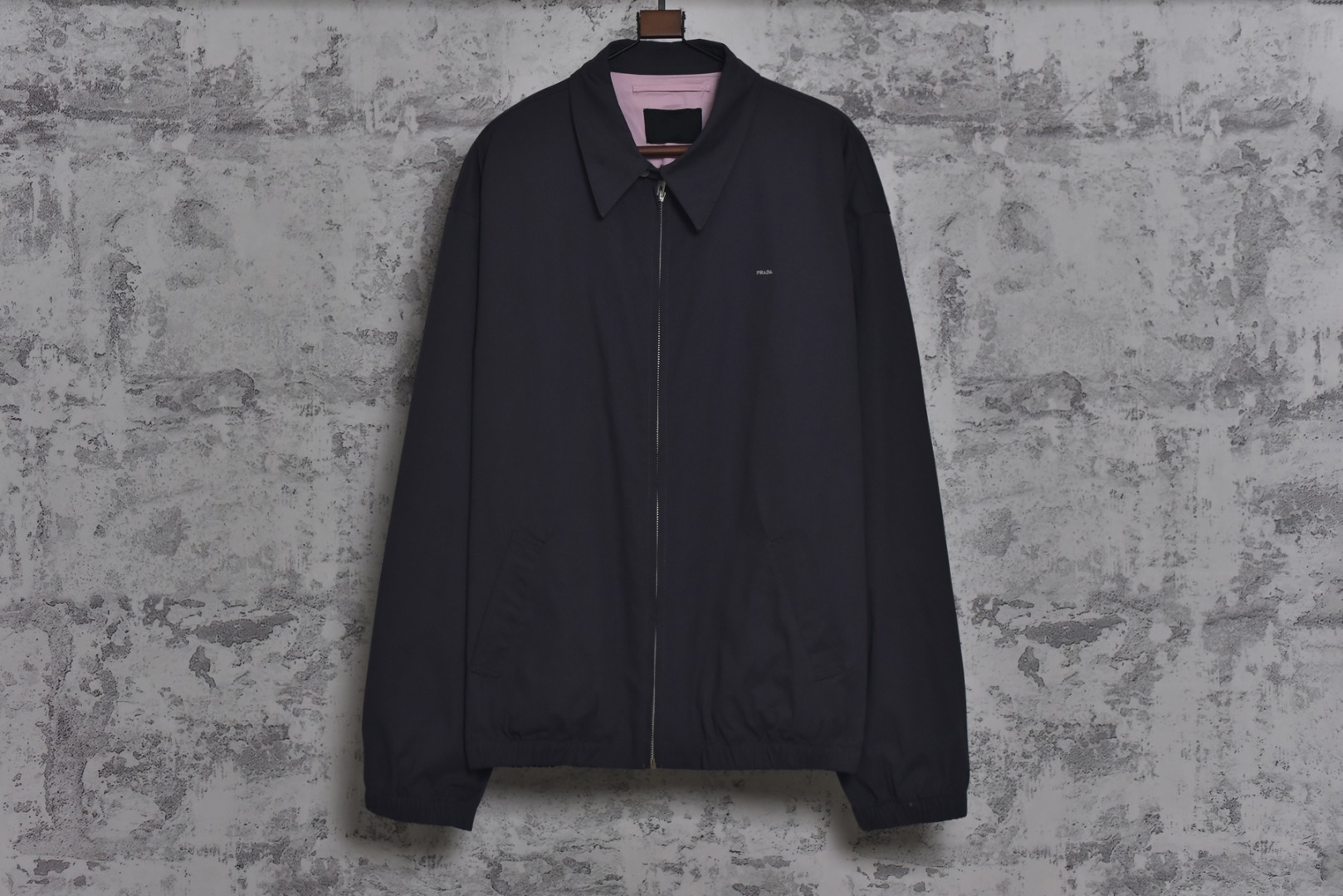 #Prada/普拉达 25Fw 小标灰粉夹克外套 定织高支高密的全工艺梭织面料，经纱与纬纱均采用精梳长绒棉与微量高科技聚酯纤维混纺，通过调整织机参数和纱线张力，使面料呈现出细腻、致密且硬挺的质感。其表面有极其细微的肌理感，而非普通面料的平淡光泽。这种密度确保了夹克廓形的立挺度与持久性，久穿不易变形。定染面料，“哈灵顿灰粉” 并非普通的粉灰色，而是经过多次校色实验的复合色调。在灰色的冷峻基调中，精准注入了一抹低饱和度的粉彩，形成了冷静克制与温柔浪漫的独特冲突感。染料采用进口环保染料，经过先染后整的工艺，色牢度极高，颜色渗透至纤维内核，确保了色彩的持久与均匀，杜绝了廉价面料的浮色感。“重机”JUKI专业缝纫设备。使用特定针距确保线迹均匀、牢固且美观。接缝均采用包边处理，完全看不到毛边，关键受力点均进行二次打结或强化，极大提升了耐用性。使用田岛多头电子刺绣机，以超过每分钟1000转的高速和0.1mm的精度还原，每一个字母的转角、弧线的边缘都清晰锐利，无任何锯齿感。定制辅料三标，男女同款 尺码：48 50 52-选品中心