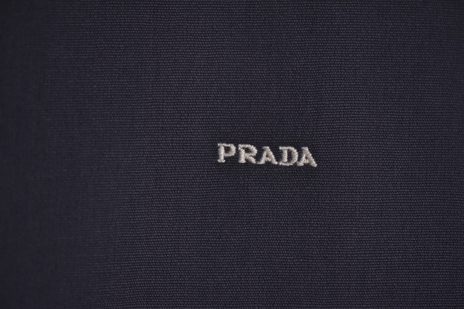 图片[3]-#Prada/普拉达 25Fw 小标灰粉夹克外套 定织高支高密的全工艺梭织面料，经纱与纬纱均采用精梳长绒棉与微量高科技聚酯纤维混纺，通过调整织机参数和纱线张力，使面料呈现出细腻、致密且硬挺的质感。其表面有极其细微的肌理感，而非普通面料的平淡光泽。这种密度确保了夹克廓形的立挺度与持久性，久穿不易变形。定染面料，“哈灵顿灰粉” 并非普通的粉灰色，而是经过多次校色实验的复合色调。在灰色的冷峻基调中，精准注入了一抹低饱和度的粉彩，形成了冷静克制与温柔浪漫的独特冲突感。染料采用进口环保染料，经过先染后整的工艺，色牢度极高，颜色渗透至纤维内核，确保了色彩的持久与均匀，杜绝了廉价面料的浮色感。“重机”JUKI专业缝纫设备。使用特定针距确保线迹均匀、牢固且美观。接缝均采用包边处理，完全看不到毛边，关键受力点均进行二次打结或强化，极大提升了耐用性。使用田岛多头电子刺绣机，以超过每分钟1000转的高速和0.1mm的精度还原，每一个字母的转角、弧线的边缘都清晰锐利，无任何锯齿感。定制辅料三标，男女同款 尺码：48 50 52-选品中心