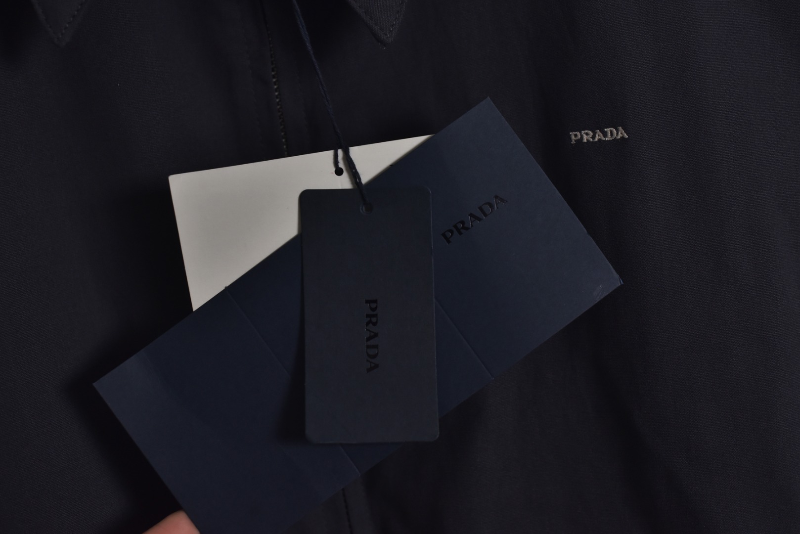 图片[7]-#Prada/普拉达 25Fw 小标灰粉夹克外套 定织高支高密的全工艺梭织面料，经纱与纬纱均采用精梳长绒棉与微量高科技聚酯纤维混纺，通过调整织机参数和纱线张力，使面料呈现出细腻、致密且硬挺的质感。其表面有极其细微的肌理感，而非普通面料的平淡光泽。这种密度确保了夹克廓形的立挺度与持久性，久穿不易变形。定染面料，“哈灵顿灰粉” 并非普通的粉灰色，而是经过多次校色实验的复合色调。在灰色的冷峻基调中，精准注入了一抹低饱和度的粉彩，形成了冷静克制与温柔浪漫的独特冲突感。染料采用进口环保染料，经过先染后整的工艺，色牢度极高，颜色渗透至纤维内核，确保了色彩的持久与均匀，杜绝了廉价面料的浮色感。“重机”JUKI专业缝纫设备。使用特定针距确保线迹均匀、牢固且美观。接缝均采用包边处理，完全看不到毛边，关键受力点均进行二次打结或强化，极大提升了耐用性。使用田岛多头电子刺绣机，以超过每分钟1000转的高速和0.1mm的精度还原，每一个字母的转角、弧线的边缘都清晰锐利，无任何锯齿感。定制辅料三标，男女同款 尺码：48 50 52-选品中心