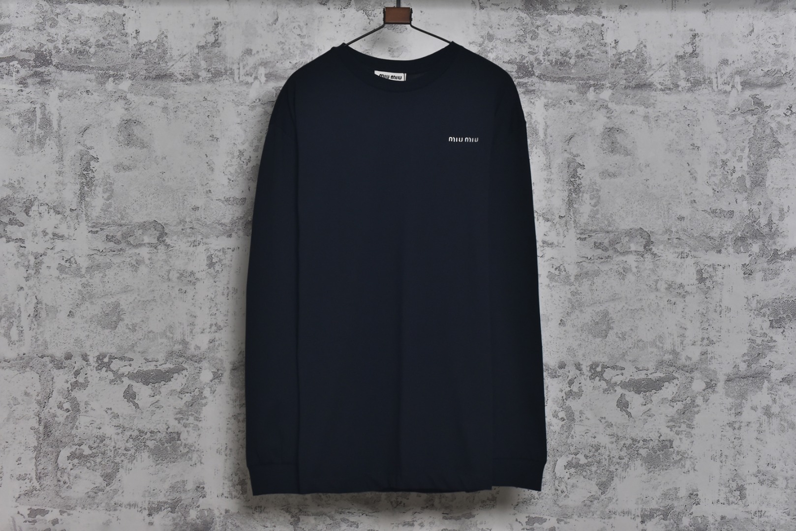 #Miu Miu 25Fw Miu小标刺绣长袖 采用高品级24支精梳棉纱线，通过「先染后织」工艺确保色彩均匀性，纱线经双股加捻提升抗起球性，布面光洁度优于普通棉织物，对版190克重精密调控：通过18针细针距圆机编织，兼顾垂坠感与挺括性，需配合恒温恒湿车间避免纱线张力波动，紧密纺结构：借鉴瑞士立达紧密纺技术，纱线毛羽减少60%，织物密度达156针/英寸²，实现婴儿肌肤触感的同时保持8%以上的弹性回复率，采用日本FIL-TEC刺绣专用涤纶线，实用进口田岛机设备，确保每英寸12针的高密度刺绣图案边缘无毛刺，底层先以水溶衬定位，中层填充天丝垫纱，表层以雕孔绣工艺打造空气感立体效果，定制辅料三标，男女同款 尺码：XS-M-选品中心