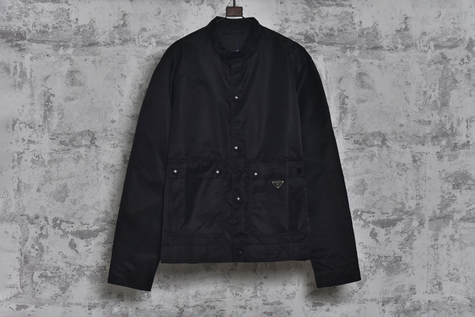 #Prada/普拉达 25Fw 双口袋三角标夹克外套 面料为特殊定制的高密度再生尼龙，并非市场普通现货，其密度、手感与防泼水性能均对标原版，力求还原Re-Nylon材质的轻盈质感与耐磨特性，原版面料重量精密控制在600-800克之间​（视款式而定），本品同样追求这种轻盈与挺括的平衡。所有五金件（包括拉链、扣具等）均源自东莞专业的箱包五金供应商，绝非普通市场通货，五金质感顺滑，经久耐用，拉链头顺滑度优异，减少卡顿感，与原版追求的耐用性一脉相承。胸前标志性的涂珐琅三角形金属徽标，采用的是与原厂（Prada供应商）一致的KF镜面三角标。此徽标由价值千万元的专用机器制作，呈现出镜面效果与清晰字体，细节精度远超市场仿品。原版徽标同样注重质感，其珐琅涂层通过盐雾测试，长期使用不易氧化。三标与洗标均为按原版材质定制，手感与材质均力求一致，确保细节处的正宗感。原版夹克在缝线工艺上采用双层缝线，拼接处使用隐藏式针脚，以提升耐用性和美观性，男女同款 尺码：46 48 50 52-选品中心