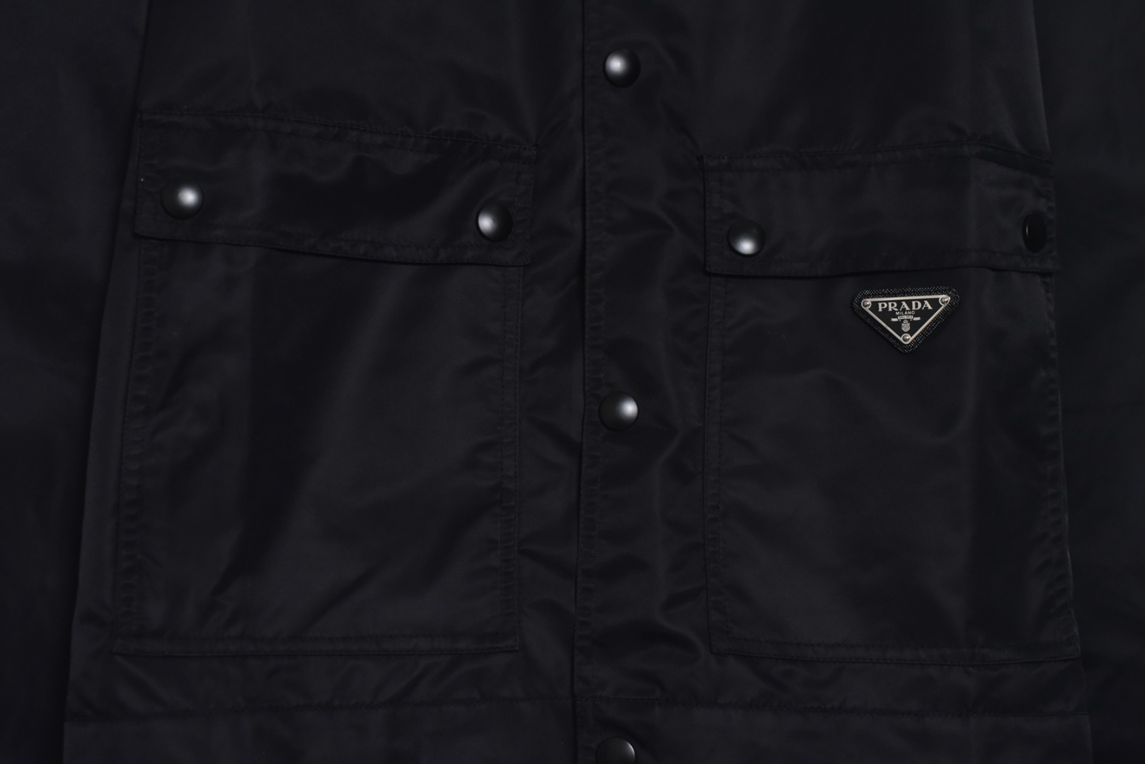 图片[5]-#Prada/普拉达 25Fw 双口袋三角标夹克外套 面料为特殊定制的高密度再生尼龙，并非市场普通现货，其密度、手感与防泼水性能均对标原版，力求还原Re-Nylon材质的轻盈质感与耐磨特性，原版面料重量精密控制在600-800克之间​（视款式而定），本品同样追求这种轻盈与挺括的平衡。所有五金件（包括拉链、扣具等）均源自东莞专业的箱包五金供应商，绝非普通市场通货，五金质感顺滑，经久耐用，拉链头顺滑度优异，减少卡顿感，与原版追求的耐用性一脉相承。胸前标志性的涂珐琅三角形金属徽标，采用的是与原厂（Prada供应商）一致的KF镜面三角标。此徽标由价值千万元的专用机器制作，呈现出镜面效果与清晰字体，细节精度远超市场仿品。原版徽标同样注重质感，其珐琅涂层通过盐雾测试，长期使用不易氧化。三标与洗标均为按原版材质定制，手感与材质均力求一致，确保细节处的正宗感。原版夹克在缝线工艺上采用双层缝线，拼接处使用隐藏式针脚，以提升耐用性和美观性，男女同款 尺码：46 48 50 52-选品中心