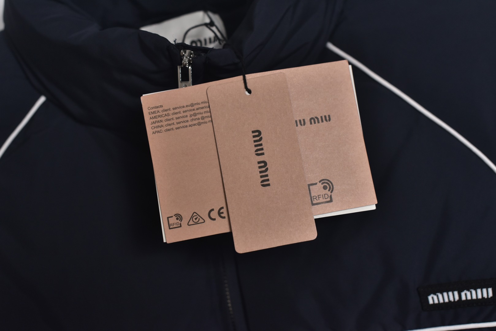 图片[9]-#Miu Miu 25Fw Miu小标捆条短款羽绒服 -核心内里填充180G广检认证90%纯白鸭绒 定制开发高支高密梭织面料，其纱线结构与织法经过精密计算，旨在实现极佳的防绒钻性，同时保证面料本身的轻盈与耐久度，面料色彩为独家定染，确保了色彩的纯粹度与独特性，采用捆条拼接工艺，该工艺在每块裁片的接缝处内衬一条白色织带，再将面料拼接并压线固定，白色的捆条在深色面料上形成了鲜明而利落的轮廓线，强化了单品的结构化视觉，内里填充90白鸭绒，高纯度绒子能锁住大量空气，形成静止空气层，实现高效保暖，这使得羽绒服在拥有极强保暖性的同时，重量得以大幅减轻，选用进口电脑充绒设备，确保每一个独立绗格内的羽绒填充量都精准、均匀，避免出现局部空洞或结块，从而保证羽绒服整体的平整度、保暖均匀性与持久蓬松，定制辅料三标 尺码：38 40 42-选品中心