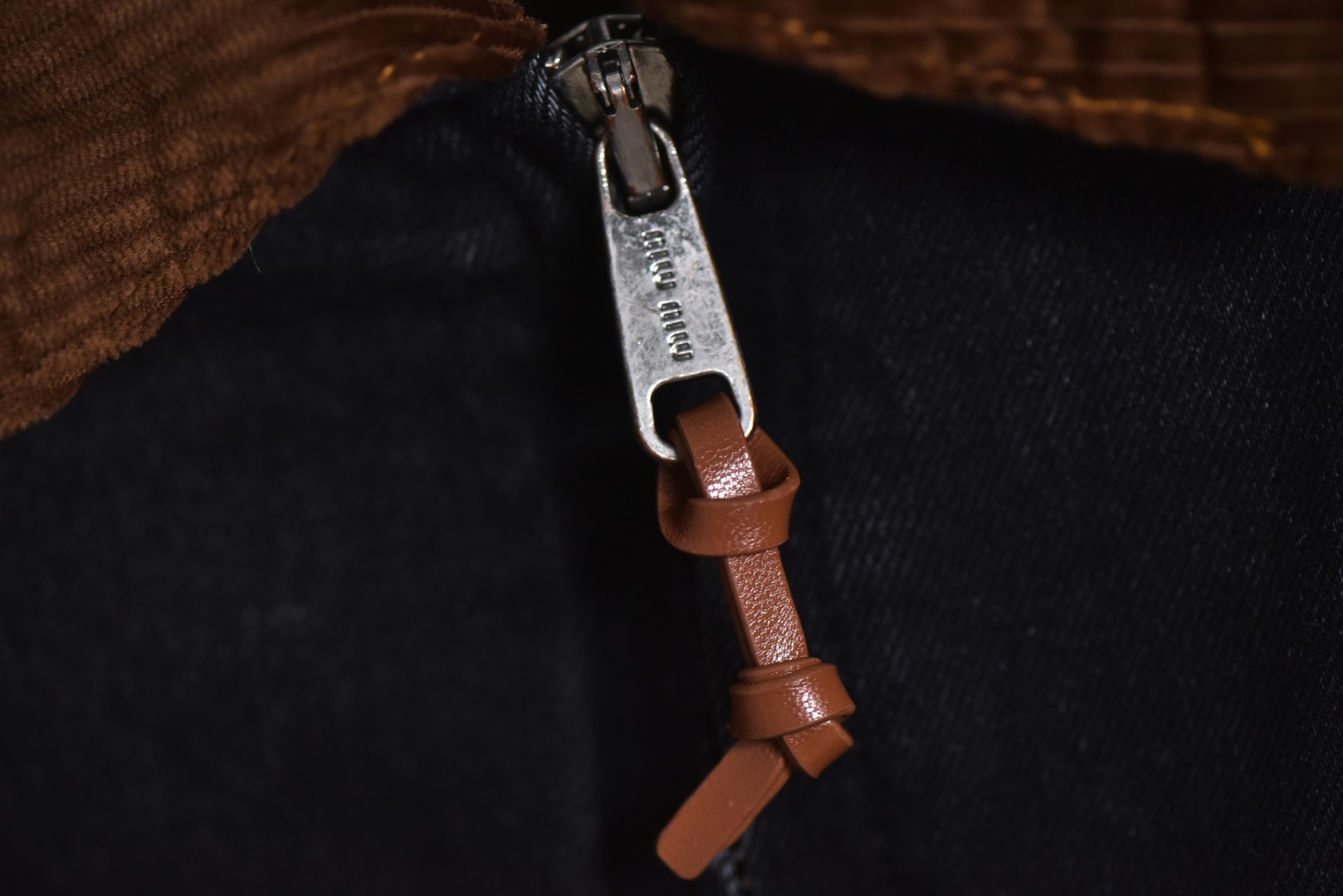 图片[4]-#Miu Miu 25Fw Miu小标牛仔棉服外套 选用高克重100%棉制牛仔斜纹布，高克重意味着面料单位面积密度更高，这不仅赋予了服装卓越的耐用性与抗皱性，更关键的是，它能自然支撑起利落而硬挺的立体廓形，无需依赖额外的内衬，面料经过专业的洗水处理，通过精准控制的酶洗、石磨等工艺，软化了原生棉布的僵硬感，使其触感更为亲肤柔顺。同时，这一过程赋予了丹宁独特的落色效果与微妙的复古做旧纹理，领部采用100%纯棉粗棱灯芯绒，其独特的瓦楞状脊线纹理与主体丹宁的斜纹肌理形成强烈而巧妙的视觉与触觉对比，将柔软且结构相对松散的灯芯绒与硬挺的牛仔布进行拼接，需要极高的裁切与缝纫精度，以确保接缝处平整牢固，避免因材质缩率不同而产生的变形。此举体现了品牌对异材质拼接工艺的成熟掌控，内里填充1400D高密度洗水棉。这里的“D”并非填充重量，而是指棉絮本身的纤维细度与长度规格，其拥有极佳的蓬松度与持久性，不易结块或移位，能确保夹克长期使用后仍保持均匀平整的保暖层，结合高克重牛仔布形成的“外壳结构”，共同构建了一个轻量却高效的隔热系统，实现了保暖性与廓形感的统一，在左前幅，运用了极为精细的真皮激光镭射雕花工艺。首先将一块小牛皮复合于面料之上，随后通过高精度激光按照预设图案进行烧蚀，刻画出品牌标识或图案，此工艺要求对激光的功率与速度进行毫厘不差的控制，才能在皮革上实现边缘锐利、细节分明的图案，同时不伤及底层的丹宁面料，定制辅料三标，男女同款 尺码：40 42 44-选品中心