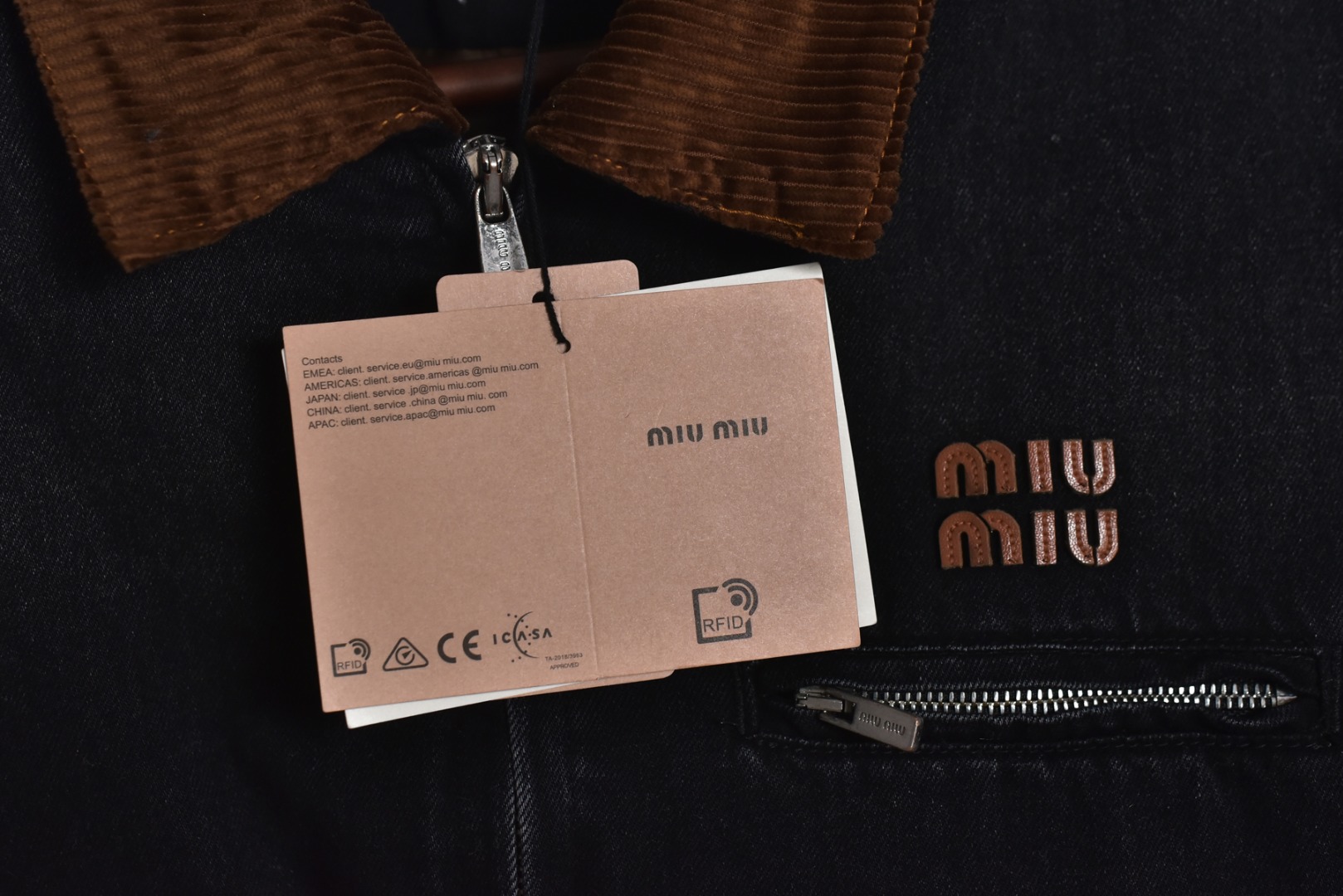 图片[8]-#Miu Miu 25Fw Miu小标牛仔棉服外套 选用高克重100%棉制牛仔斜纹布，高克重意味着面料单位面积密度更高，这不仅赋予了服装卓越的耐用性与抗皱性，更关键的是，它能自然支撑起利落而硬挺的立体廓形，无需依赖额外的内衬，面料经过专业的洗水处理，通过精准控制的酶洗、石磨等工艺，软化了原生棉布的僵硬感，使其触感更为亲肤柔顺。同时，这一过程赋予了丹宁独特的落色效果与微妙的复古做旧纹理，领部采用100%纯棉粗棱灯芯绒，其独特的瓦楞状脊线纹理与主体丹宁的斜纹肌理形成强烈而巧妙的视觉与触觉对比，将柔软且结构相对松散的灯芯绒与硬挺的牛仔布进行拼接，需要极高的裁切与缝纫精度，以确保接缝处平整牢固，避免因材质缩率不同而产生的变形。此举体现了品牌对异材质拼接工艺的成熟掌控，内里填充1400D高密度洗水棉。这里的“D”并非填充重量，而是指棉絮本身的纤维细度与长度规格，其拥有极佳的蓬松度与持久性，不易结块或移位，能确保夹克长期使用后仍保持均匀平整的保暖层，结合高克重牛仔布形成的“外壳结构”，共同构建了一个轻量却高效的隔热系统，实现了保暖性与廓形感的统一，在左前幅，运用了极为精细的真皮激光镭射雕花工艺。首先将一块小牛皮复合于面料之上，随后通过高精度激光按照预设图案进行烧蚀，刻画出品牌标识或图案，此工艺要求对激光的功率与速度进行毫厘不差的控制，才能在皮革上实现边缘锐利、细节分明的图案，同时不伤及底层的丹宁面料，定制辅料三标，男女同款 尺码：40 42 44-选品中心