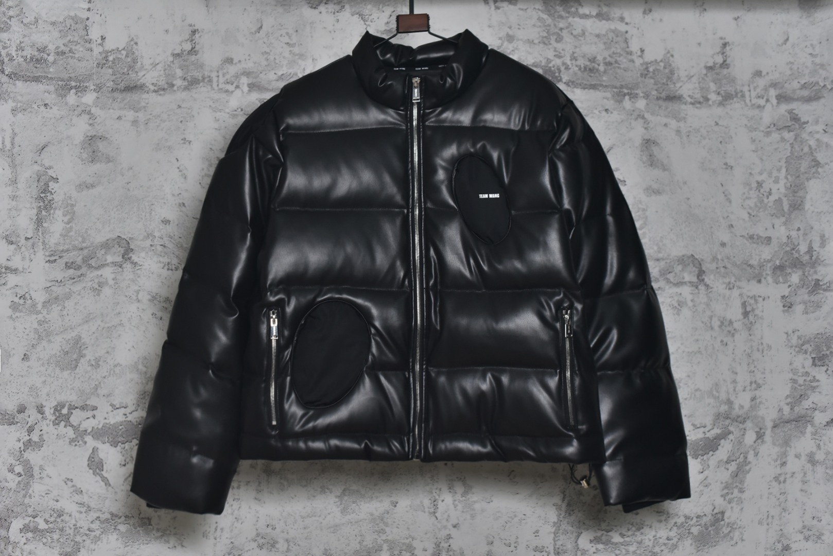 #Team Wang 初代字母皮革立领羽绒服 -内里填充90白鸭绒，0码填充200克，1码填充220克，2码填充240克 -注：皮革材质的羽绒服洗涤需送至干洗店清洗，切记切记切记 一件好的单品应能融入多种生活场景，并易于打理以保持最佳状态，本次推出的羽绒服，可以看作是这一理念在实用主义单品上的投射，内填充物符合新国标90%白鸭绒标准，绒子含量高，蓬松度优异，能有效锁住空气，隔绝寒冷，由专业大厂加工，采用先进工艺严防跑绒。特别定制600克高克重袖子螺纹，确保多次洗涤后袖口仍保持版型，不变形、不松弛，主打利落的短款版型，旨在拉长身材比例，五金件的拉链、拉头、鸡眼等均注重质感，全部开模定制顺滑耐用，充绒量根据尺码递增确保不同体型穿着者都能获得合身的保暖体验，男女同款 尺码：0 1 2-选品中心