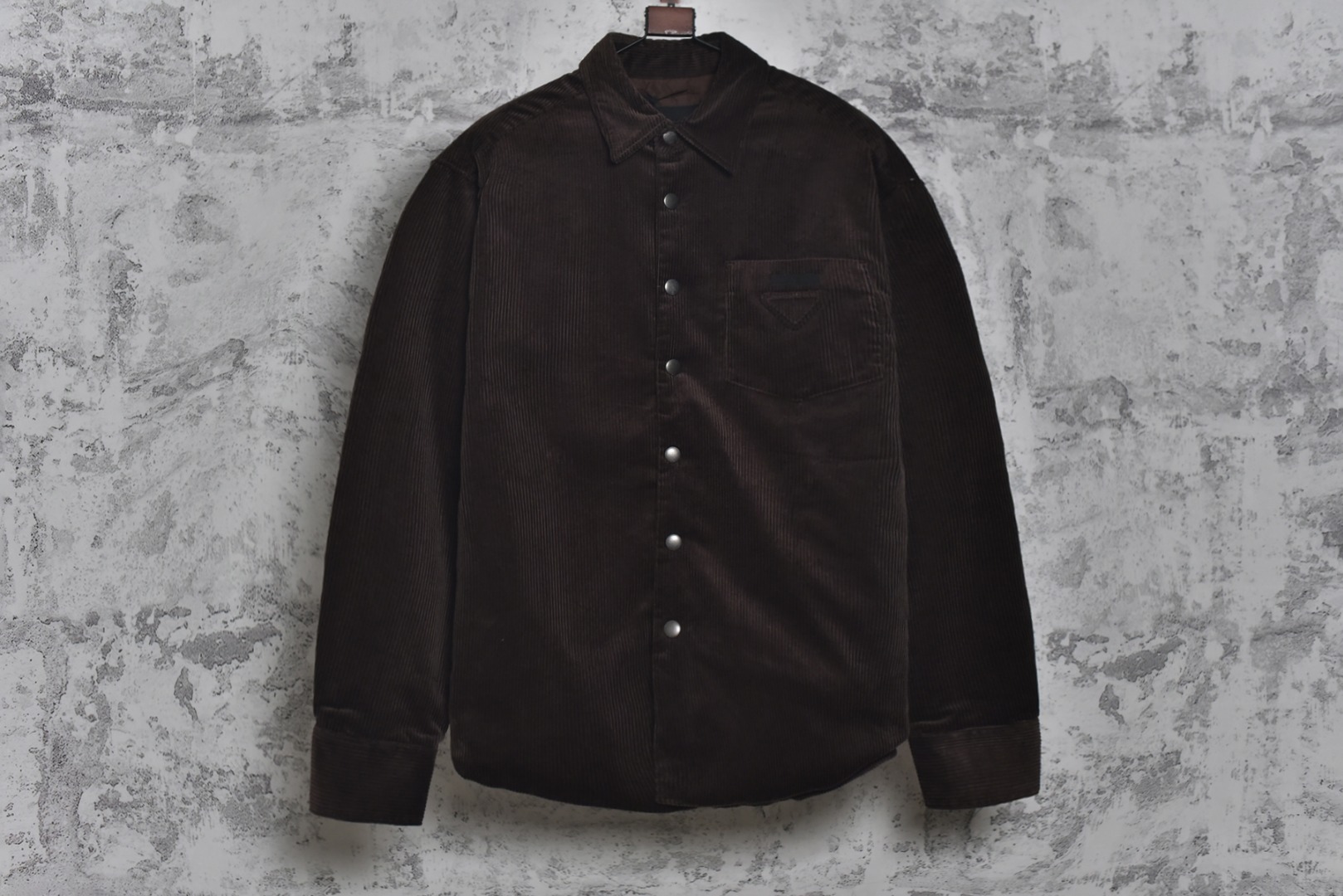 #PRD灯芯绒贴布棉服 深棕色 乌木色款为100%棉 填充层为55%再生聚酯纤维+45%聚酯纤维 采用Prada 2025秋冬新配方 将传统灯芯绒克重从380g/㎡降至260g/㎡ 兼顾透气性与挺括度 经纱选用28tex×2（21/2英支）股线 纬纱为28tex（21英支）单纱 符合高端灯芯绒纱线规格 成品克重260g/㎡ 属于轻盈型灯芯绒 绒条细腻且回弹无褶 整体采用压胶工艺替代传统平车踩线，接缝处密封性好，且减少线迹磨损风险 面料经过预洗水+软整理 绒面手感柔软且无浮色 色牢度达ISO 105标准4级以上 尺码：XS S M L-选品中心