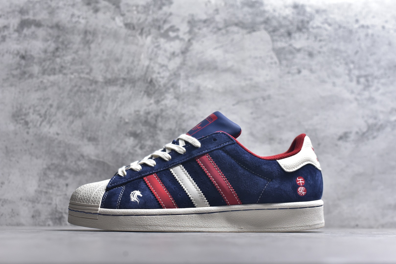 #经典贝壳 马年焕新ADIDAS SUPERSTAR 藏蓝翻毛皮质感升级，红白撞色三条纹活力吸睛，鞋侧骏马刺绣与“千马”印章暗藏新年巧思。贝壳头设计延续街头基因，软弹橡胶底适配日常穿搭，既是复古潮人的情怀之选，也是春节走亲访友的吸睛利器。 货号：JY8925 尺码：36 36.5 37.5 38 38.5 39 40 40.5 41 42 42.5 43 44 44.5 45-选品中心