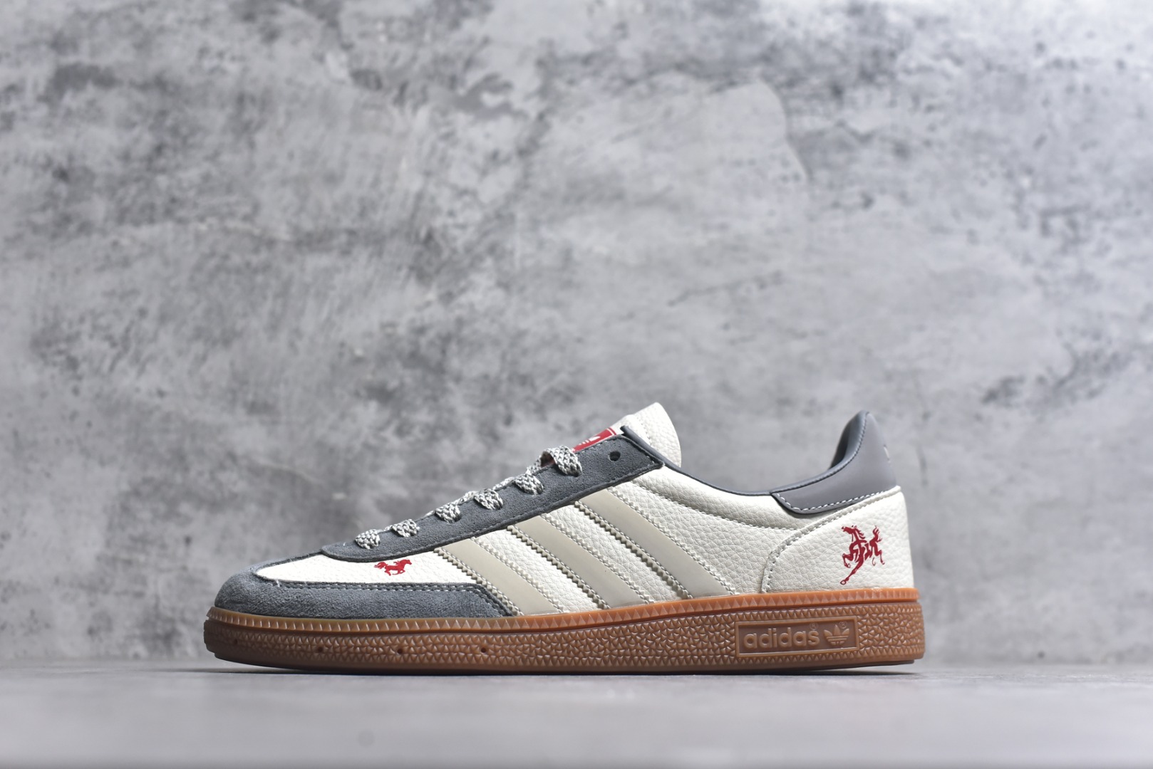 #马年新款海外定制限量发售 Adidas Originals GAZELLE INDOOR“马年联名限定-白灰”专为 2026 丙午马年打造的限定德训鞋，延续 adidas 经典板鞋版型，鞋尾与鞋头均点缀红色骏马剪影刺绣，身主体为米白荔枝纹皮革，搭配雾灰磨砂皮鞋头、浅灰三道杠及同色系鞋尾，标志性生胶外底加持，荔枝皮鞋面柔软亲肤，橡胶防滑大底稳当贴脚 货号：ZH2605 尺码：36 36.5 37.5 38 38.5 39 40 40.5 41 42 42.5 43 44 44.5 45-选品中心