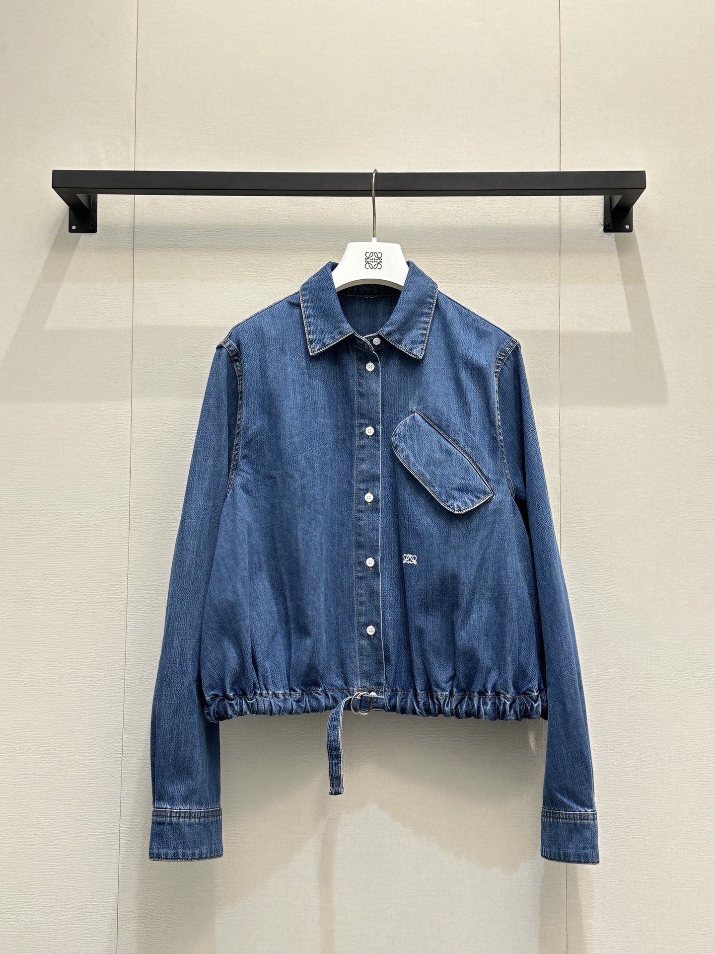 NO:805363,Loewe26's new model adopts a balloon silhouette (lantern silhouette) short cut. The hem can be freely adjusted through a D-ring drawstring. It can not only create an elastic pleat effect, but also tighten the waistline to optimize the proportion. It is very tolerant to the body shape. The diagonal flap pocket on the chest is the key design that distinguishes it from ordinary denim shirts.  Logo embroidery on the front highlights the brand logo in a low-key manner. Washed denim fabric has a soft and distressed texture, which is soft but not collapsed, taking into account both comfort and stiffness. The classic lapel + front button closure, paired with French cuffs, retain the neatness of the shirt, while using the silhouette and drawstring to inject a casual and relaxed atmosphere. Pair it with high-waisted straight jeans and white shoes for casual daily use, creating a refreshing American retro style.  Wear a white suspender/white T inside, unbutton a few buttons on the collar, and pair it with suit pants and loafers, which is relaxed and smart. Wear it as a thin coat open, paired with a dress or wide-leg pants to increase the layering of the outfit. SML real photos of large products, loewe, loafers, skirts, jeans, jackets & coats, shirts, business suit,19860909Loewe26新款 采用气球廓形（灯笼轮廓）短款剪裁,下摆通过D形环抽绳可自由调节,既能打造松紧褶皱效果,也能收紧腰线优化比例,对身材的包容度很高. 胸前的对角翻盖口袋,是区别于普通牛仔衬衫的关键设计. 正面logo刺绣,低调点明品牌识标.水洗牛仔面料,自带柔和做旧质感,软而不塌,兼顾舒适度与挺括度.经典翻领+前襟纽扣开合,搭配法式袖口,保留了衬衫的利落感,同时用廓形和抽绳注入了休闲松弛的氛围.休闲日常搭配高腰直筒牛仔裤+小白鞋,打造清爽的美式复古风. 内搭白色吊带/白T,解开领口几颗纽扣,搭配西装裤+乐福鞋,松弛又干练. 作为薄外套敞开穿,搭配连衣裙或阔腿裤,增加穿搭层次感.SML大货实拍,,loewe,loafers,skirts,jeans,jackets & coats,shirts,business suit,,Women's clothing