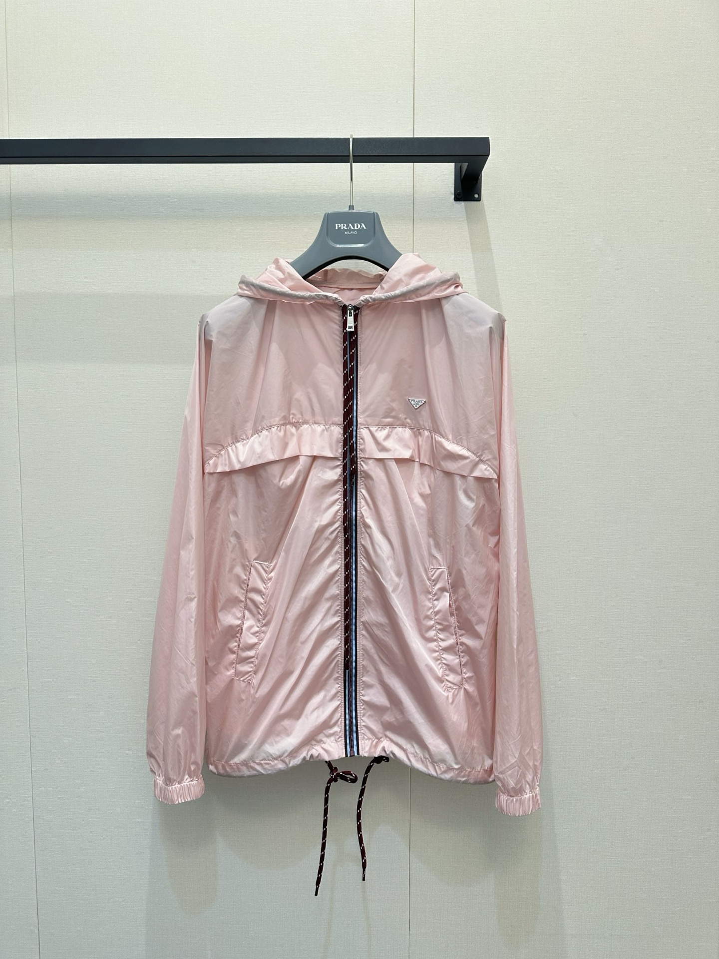 NO:834234,Prada  Light pink hooded lightweight jacket. This Prada light pink hooded lightweight jacket is made of high-woven fine regenerated nylon or polyester amine fiber fabric. It is light, smooth and has a soft luster. It is windproof, water-repellent and sun-proof. The loose shoulder silhouette is not flattering. The burgundy drawstrings on the hood and hem can be freely adjusted for tightness. The front contrast stripe zipper and the iconic enamel on the chest.  Details such as the enamel triangular metal logo, zipper pockets on both sides and elastic cuffs not only retain the clean texture of the brand, but also add practicality and beauty. It is suitable for daily leisure, commuting or outdoor travel. It can be used as a sun protection/windproof jacket in spring and summer, and as a layering item in early autumn. The soft light pink color is gentle and white, and can be easily matched with jeans, prada, and jackets.  & coats,jackets & coats,hats,19860909Prada 浅粉色连帽轻薄夹克,这件Prada浅粉色连帽轻薄夹克,采用高织细腻的再生尼龙或聚酯胺纤维面料,轻盈爽滑且带有柔和光泽,兼具防风、防泼水与防晒功能；宽松落肩廓形不挑身材,连帽与下摆的酒红色抽绳可自由调节松紧,正面撞色条纹拉链、胸前标志性涂珐琅三角形金属徽标、两侧拉链口袋及松紧收口袖口等细节,既保留了品牌利落质感,又增添了实用与美观性.它适合日常休闲、通勤或户外出行,春夏季可作防晒/防风外套,早秋可作叠穿单品,柔和浅粉色调温柔显白,能轻松搭配牛仔,,prada,jackets & coats,jackets & coats,hats,,Women's clothing