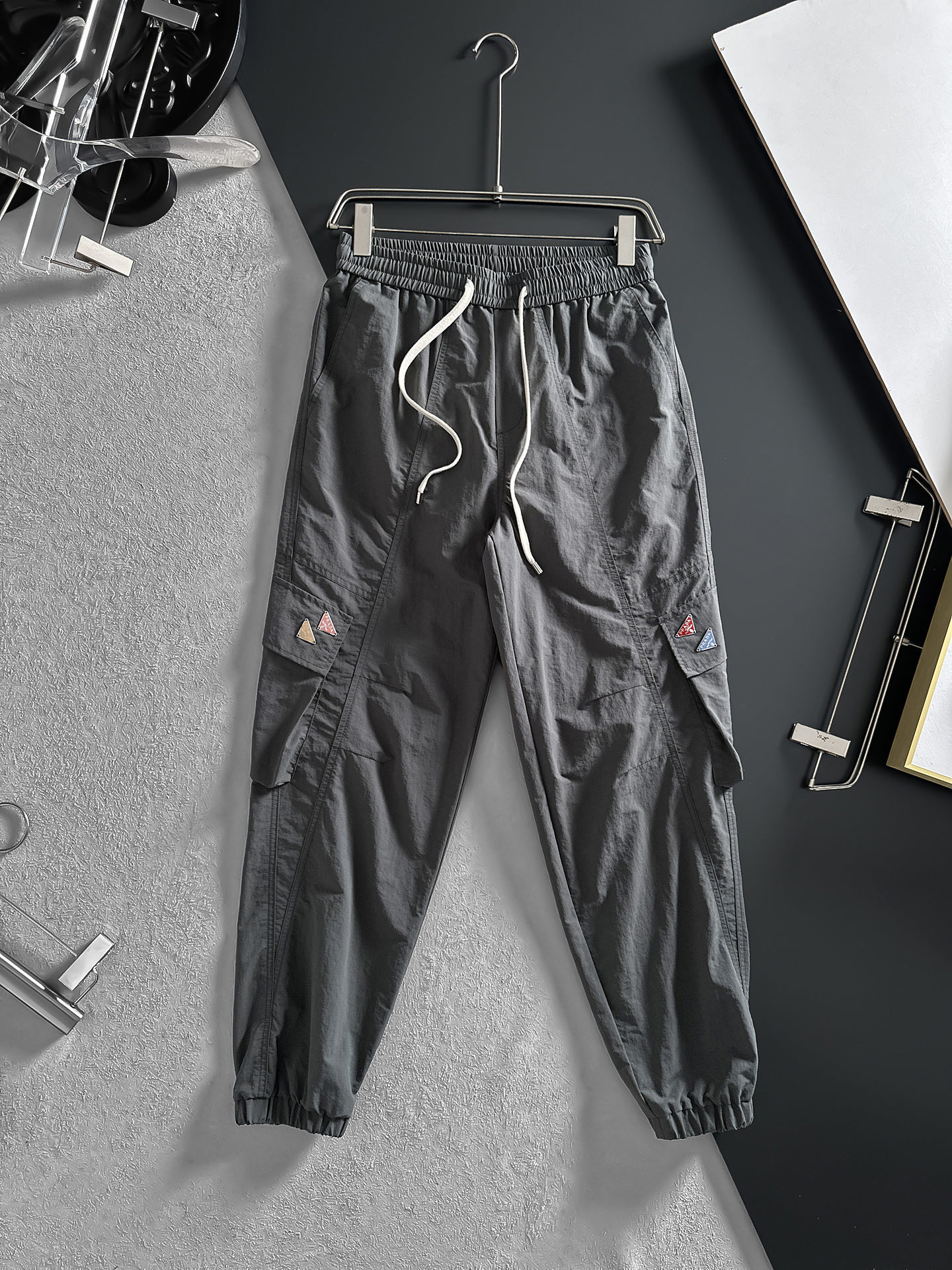 NO:870724,PRADA Dark Gray Workwear Trousers | Both cool and practical. You can never go wrong with classic dark gray, which is both slim and versatile. The loose fit and drawstring design allow you to adjust the tightness according to your own preferences, giving you perfect comfort.  Multiple large pockets on both sides are super practical and convenient for placing small items. The high-end customized P family’s classic triangular rainbow logo adds a bit of coolness. The leg-tie style makes the overall look neater. Size M-4XL (shipped next day),, prada, prada,19860909PRADA普拉达 深灰工装束脚裤 | 酷感与实用兼具 经典深灰永远不会出错,既显瘦又百搭.宽松的版型加上抽绳设计,能根据自己的喜好调节松紧,舒适度满分. 两侧多个大口袋超实用,方便放置小物件,高端定制之P家经典三角彩虹色logo,增添了几分酷感.束脚的款式让整体造型更利落.码数M-4XL（隔天出货）,,prada,prada,,Men's clothing