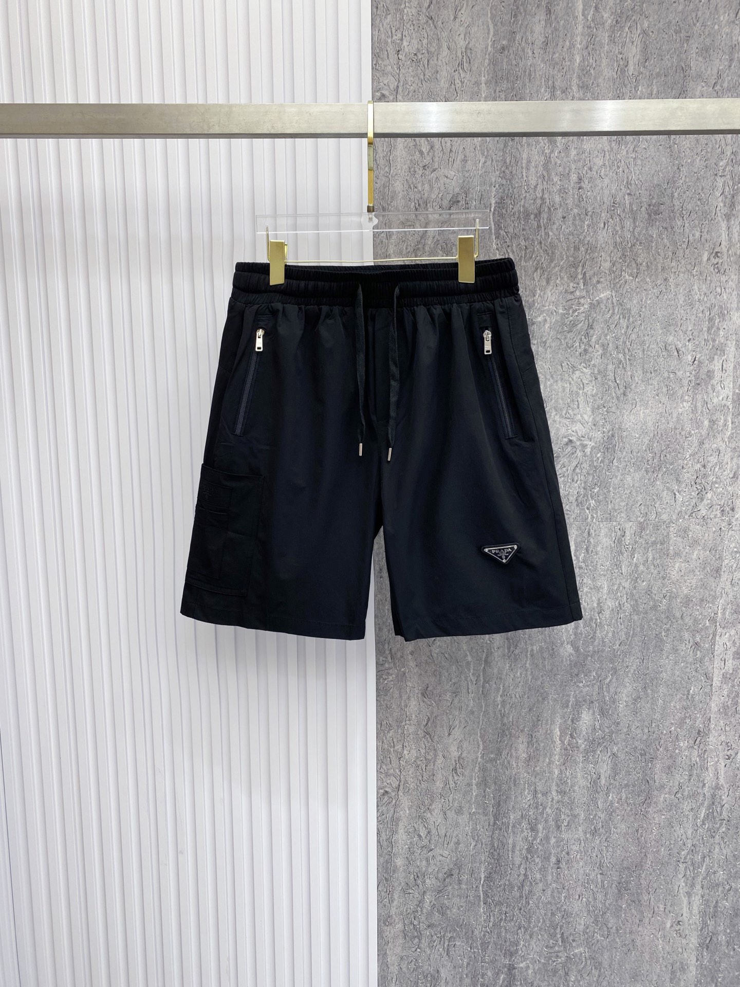 NO:842812,Prada Prada  2026ss summer classic triangle logo functional shorts, reconstructing summer casual aesthetics with minimalist lines. High-density anti-wrinkle nylon fabric is selected, which is smooth to the touch and has excellent breathability. It is light and burdenless to wear in summer; the elastic drawstring design at the waist is suitable for various body shapes and can be matched with  Equipped with double zipper side pockets and three-dimensional work patch pockets, the storage is full of security. The iconic enamel triangle logo on the front is the finishing touch, the webbing logo on the back has rigorous details, and the neat straight silhouette modifies the leg shape. Whether you are commuting in the city or traveling outdoors, you can easily create a high-end sense of relaxation.  Color Black White Size 48-56, prada, prada, shorts,19860909Prada 普拉达 2026ss夏季经典三角标机能短裤,以极简线条重构夏日休闲美学.甄选高密抗皱锦纶面料,触感顺滑且具备极佳透气性,夏日穿着轻盈无负担；腰头弹力抽绳设计适配各种身形,搭配双拉链侧袋与立体工装贴袋,收纳安全感拉满.正面标志性珐琅三角徽标点睛,背面织带标细节严谨,利落直筒版型修饰腿型,无论是都市通勤还是户外出行,皆能轻松演绎高阶松弛感. 颜色黑色 白色 码数48-56,,prada,prada,shorts,,Men's clothing