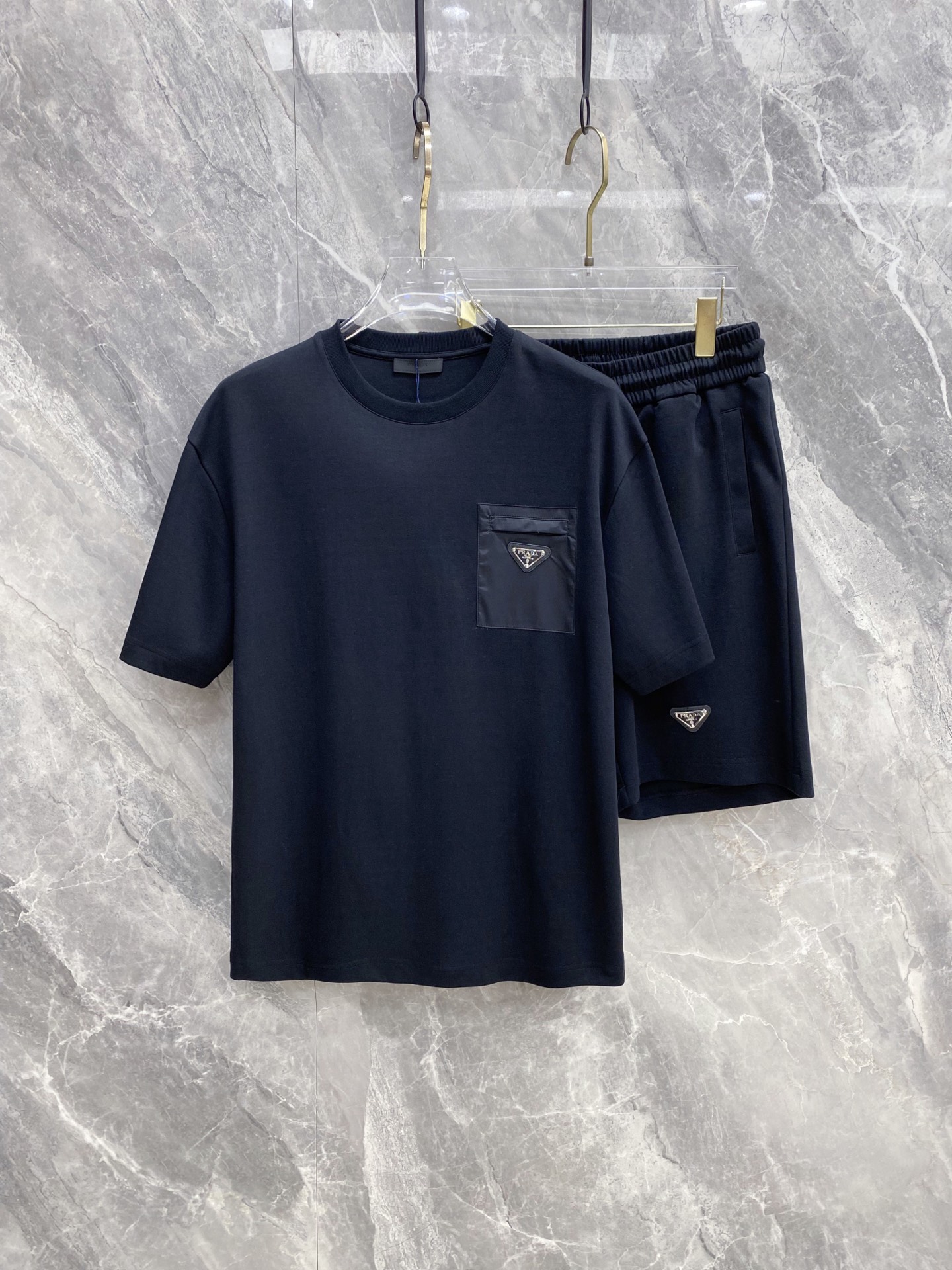 NO:861079,/ Set Prada 1911 Spring and Summer | Prada Triangle Pocket Set A set that captures the 'effortless sense of luxury'. The T-shirt is made of soft, skin-friendly high-count cotton, paired with tencel-like drape shorts of the same color. The nylon stitching on the pocket + the iconic triangle logo are low-key and recognizable. Available in black and white, the white is refreshing and clean, and the black is neat and cool. The whole set is effortless to wear out, relaxed and elegant.  Size 48-56,,prada,prada,shorts,tees,t-shirt,19860909/套 Prada 普拉达1911 春夏｜Prada 三角标口袋套装 一套把“不费力的高级感”拿捏了. T恤是软糯亲肤的高支棉,搭配同色系天丝感垂坠短裤,口袋处的尼龙拼接+标志性三角标,低调又有辨识度. 黑白两色,白的清爽干净,黑的利落酷感,整套穿出门不用费脑搭配,松弛又显贵. 码数48-56,,prada,prada,shorts,tees，t-shirt,,Men's clothing