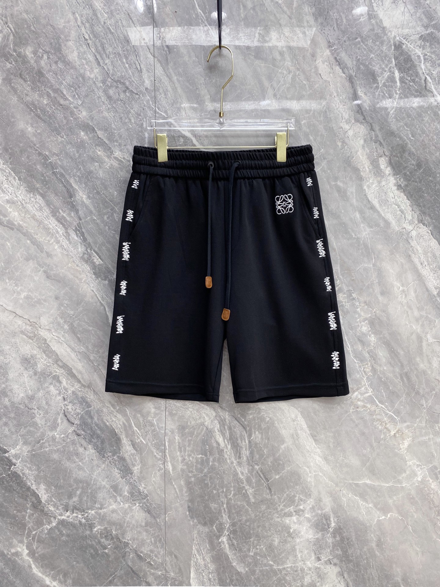 NO:861048,| LOEWE 2026 spring and summer new style casual sweatpants with side embroidery, a must-have item for spring and summer with a lazy old-money style, iconic Anagram embroidery + side hand-stitching, low-key highlighting the brand style, and full of relaxation. Selected high-weight breathable terry fabric, the upper body is soft and skin-friendly, has a cool feeling without sweating, and is draped and stylish without looking bloated.  The elastic drawstring waistband with genuine leather decorative details has a full texture, adapts to a variety of body shapes, and has zero constraints for daily wear. Practical pockets on both sides take into account both appearance and practicality. Available in three colors: off-white/hemp gray/black, it is easy to control casual, sophisticated and commuting styles. It can match your wardrobe throughout the summer. Size 48~56,,loewe,loewe,19860909| LOEWE 罗意威 2026春夏新款 侧边刺绣休闲卫裤 自带慵懒老钱风的春夏刚需单品,标志性Anagram刺绣+侧边手工缝线,低调彰显品牌格调,把松弛感拉满 甄选高克重透气毛圈面料,上身软糯亲肤,自带凉感不闷汗,垂坠有型不显臃肿 松紧抽绳腰头搭配真皮装饰细节,质感拉满,适配多种身形,日常穿零束缚 双侧实用口袋兼顾颜值与实用性,米白/麻灰/黑三色可选,轻松驾驭休闲、轻熟、通勤多种风格,承包你整个夏天的衣柜搭配 码数48~56,,loewe,loewe,,Men's clothing