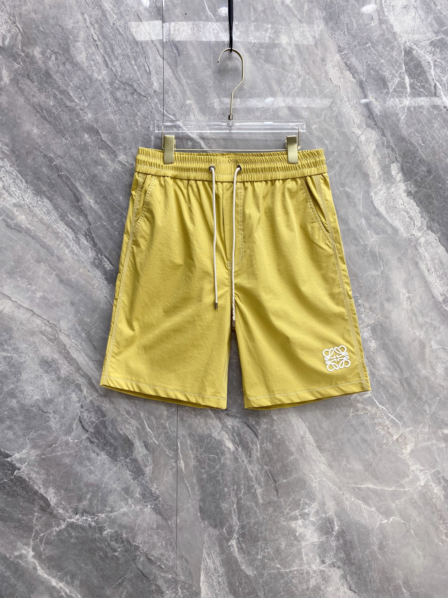 NO:860985,| LOEWE 2026 spring and summer new top-stitched embroidered casual shorts are a must-have spring and summer item with a refreshing and relaxed feel. Contrasting top-stitching outlines the outline + iconic Anagram embroidery, which completes the minimalist sense of luxury. Selected breathable and quick-drying fabrics, the upper body has a cool feeling, drape is refreshing and non-stick to the legs, loose tailoring hides the flesh and is neat. Elastic drawstring waist design, adapts to a variety of body shapes, and has no sense of restraint in daily wear.  The practical pockets on both sides take into account both appearance and practicality, and are available in three colors: white/turmeric/black. You can easily control casual, sophisticated, and vacation styles, and can provide you with refreshing outfits throughout the summer. Size 48~56,,loewe,loewe,shorts,19860909| LOEWE 罗意威 2026春夏新款 明线刺绣休闲短裤 自带清爽松弛感的春夏刚需单品,撞色明线勾勒轮廓+标志性Anagram刺绣,把极简高级感拉满 甄选透气速干面料,上身自带凉感,垂坠清爽不粘腿,宽松剪裁藏肉又利落 松紧抽绳腰头设计,适配多种身形,日常穿零束缚感 双侧实用口袋兼顾颜值与实用性,白/姜黄/黑三色可选,轻松驾驭休闲、轻熟、度假多种风格,承包你整个夏天的清爽穿搭 码数48~56,,loewe,loewe,shorts,,Men's clothing