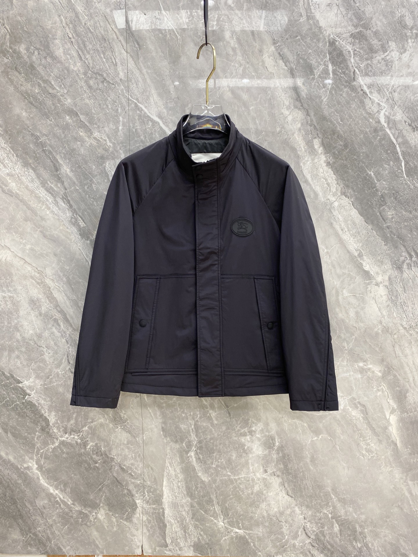 NO:956610,Burberry 2026 Autumn and Winter minimalist stand-up collar thin cotton commuter jacket. High-density anti-wrinkle and windproof woven fabric, matte navy blue, low-key and calm, neat and not bulky upper body. Simple stand-up collar with double snap button + zipper closure, small round leather logo on the chest, restrained and elegant. Symmetrical double pockets with concealed button design. Raglan sleeves are cut without binding the arms, allowing for freedom of movement.  Thin quilted filling, light and heat-locking, does not compress the body shape, suitable for business commuting and daily travel. No unnecessary and complicated design, versatile and just needed by mature men, same style for men and women, size M-3XL,, burberry, burberry, jackets & coats,19860909Burberry 巴宝莉 2026秋冬极简立领薄棉通勤夹克 高密抗皱防风梭织面料,哑光藏青色低调沉稳,上身利落不臃肿 简约立领门襟按扣+拉链双重开合,胸口圆形皮质小标点缀,克制显贵 对称双插袋搭配暗扣设计,插肩袖剪裁不束缚手臂,活动自在 薄夹棉填充,轻盈锁温,不压身形,商务通勤、日常出行都适配 无多余繁杂设计,成熟男士百搭刚需,男女同款 码数M-3XL,,burberry,burberry,jackets & coats,,Men's clothing