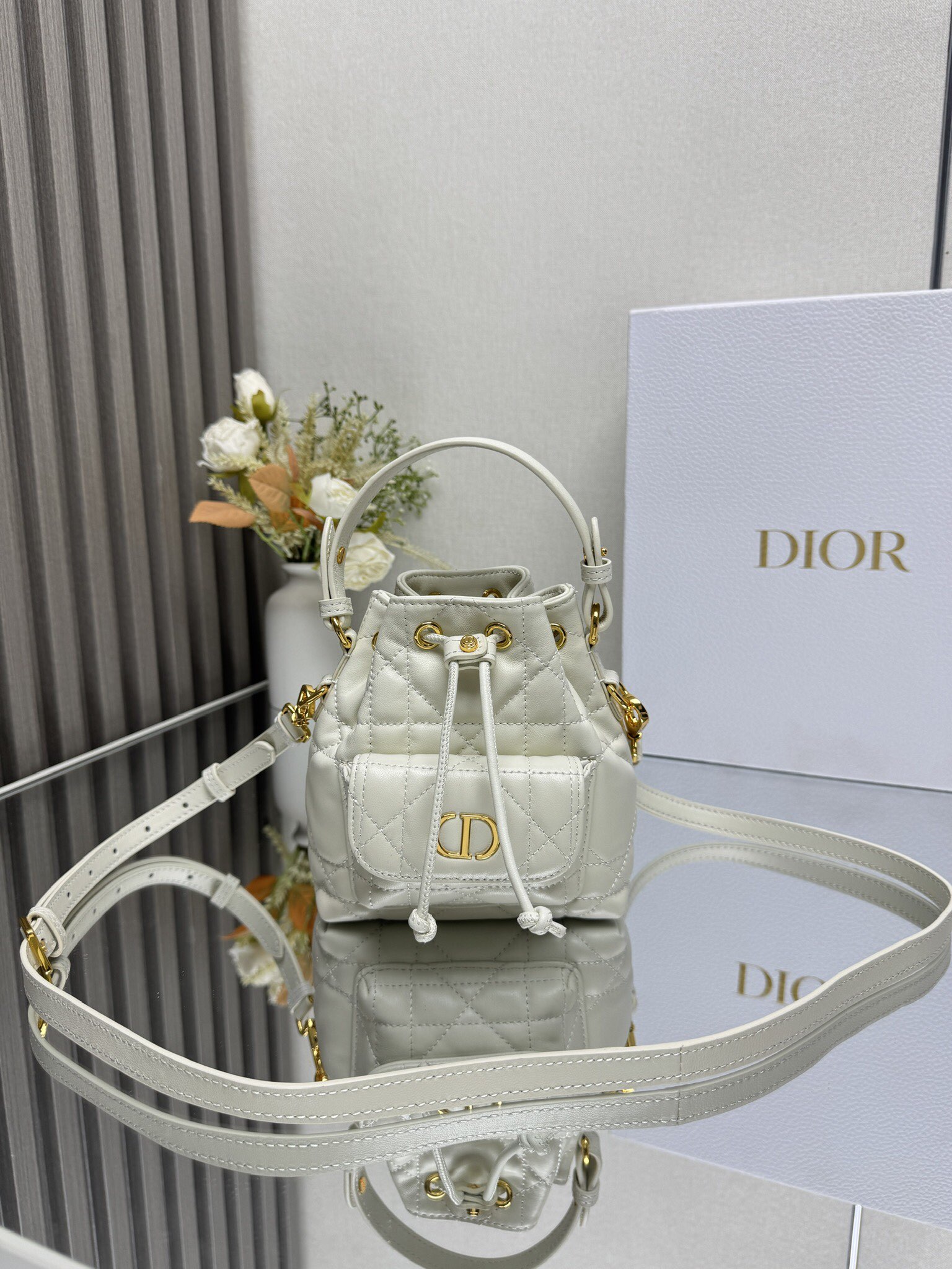 NO:659355,This miniature Dior Caro bucket bag is a new addition to the Fall 2025 ready-to-wear collection, emphasizing fashionable elegance. It is crafted from black sheepskin, decorated with oversized cannage pattern topstitching, and has a drawstring compartment. The front flap pocket is decorated with a vintage gold-finish metal CD logo, which can store a variety of small daily necessities. Fashionable and versatile, with a detachable top handle and an adjustable and detachable shoulder strap, it can be carried by hand, shoulder or cross-body.  CD logo drawstring closure on the front Magnetic flap pocket on the front Internal slip pocket Detachable leather handle on top Adjustable, detachable leather shoulder strap with dust bag included Size 14*15*7cm Made in Italy Model: Mini off-white 000550, Dior, dior, dior, sheepskin19860909这款微型 Dior Caro 水桶包是二零二五秋季成衣系列新品,彰显时尚优雅风范.采用黑色羊皮革精心制作,饰以超大藤格纹缉面线,设有一个抽绳隔层.正面翻盖口袋饰以复古金色饰面金属CD 标志,可收纳各种小件日常用品.时尚百搭,搭配可拆卸顶部手柄和可调节、可拆卸的肩带,可手提、肩背或斜挎. 正面饰以CD标志抽绳开合 正面磁性翻盖口袋内部插袋 顶部可拆卸皮革手柄 可调节、可拆卸的皮革肩带内含防尘袋 尺寸14*15*7cm 意大利制造 型号: 迷你米白色 000550,迪奥,dior,dior,sheepskin,Bag