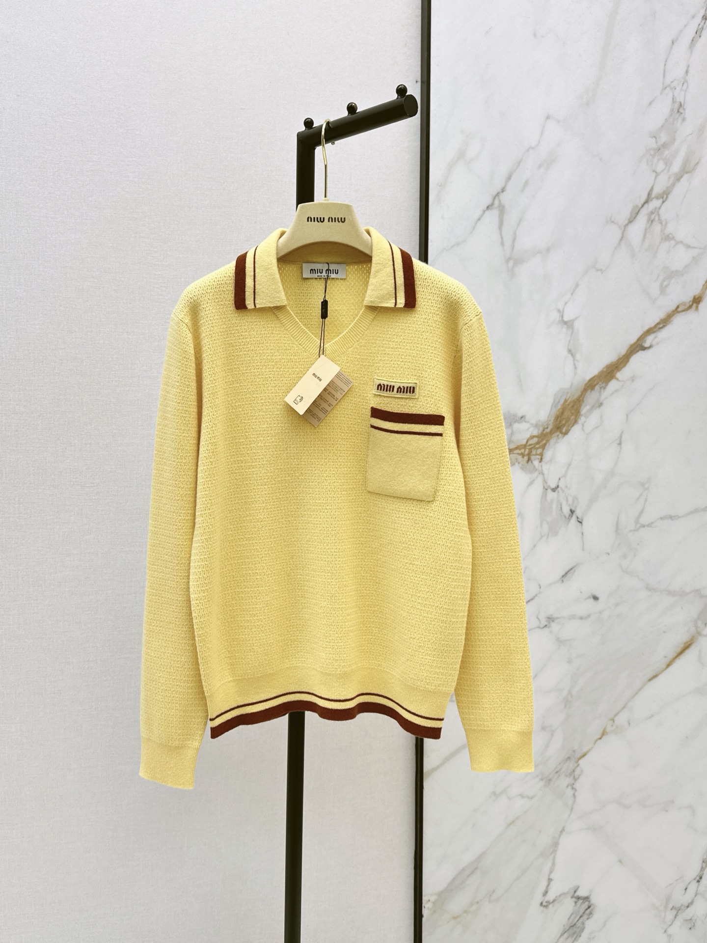 NO:958570,Miu 26Ss - the latest early autumn contrasting Polo collar hollow knitted top, bright goose yellow and white, retro college style contrasting stripe design, full of atmosphere. Polo V-neck version. Collar pocket hem with brown and red double line stripes. Exquisite layers. Breathable hollow knitted weave. The fabric is light and soft. The left patch pocket is equipped with a woven label letter logo. Full sense of details. One color sml,,miumiu,19860909Miu 26Ss————早秋最新款撞色Polo领镂空针织上衣明亮鹅黄色元气显白 复古学院风撞色条纹设计 氛围感十足 Polo V领版型 领边口袋下摆搭配棕红双线条纹 层次精致 透气镂空针织织法 面料轻盈软糯 左侧贴袋搭配织唛字母标识 细节感拉满 一色sml,,miumiu,,Women's clothing