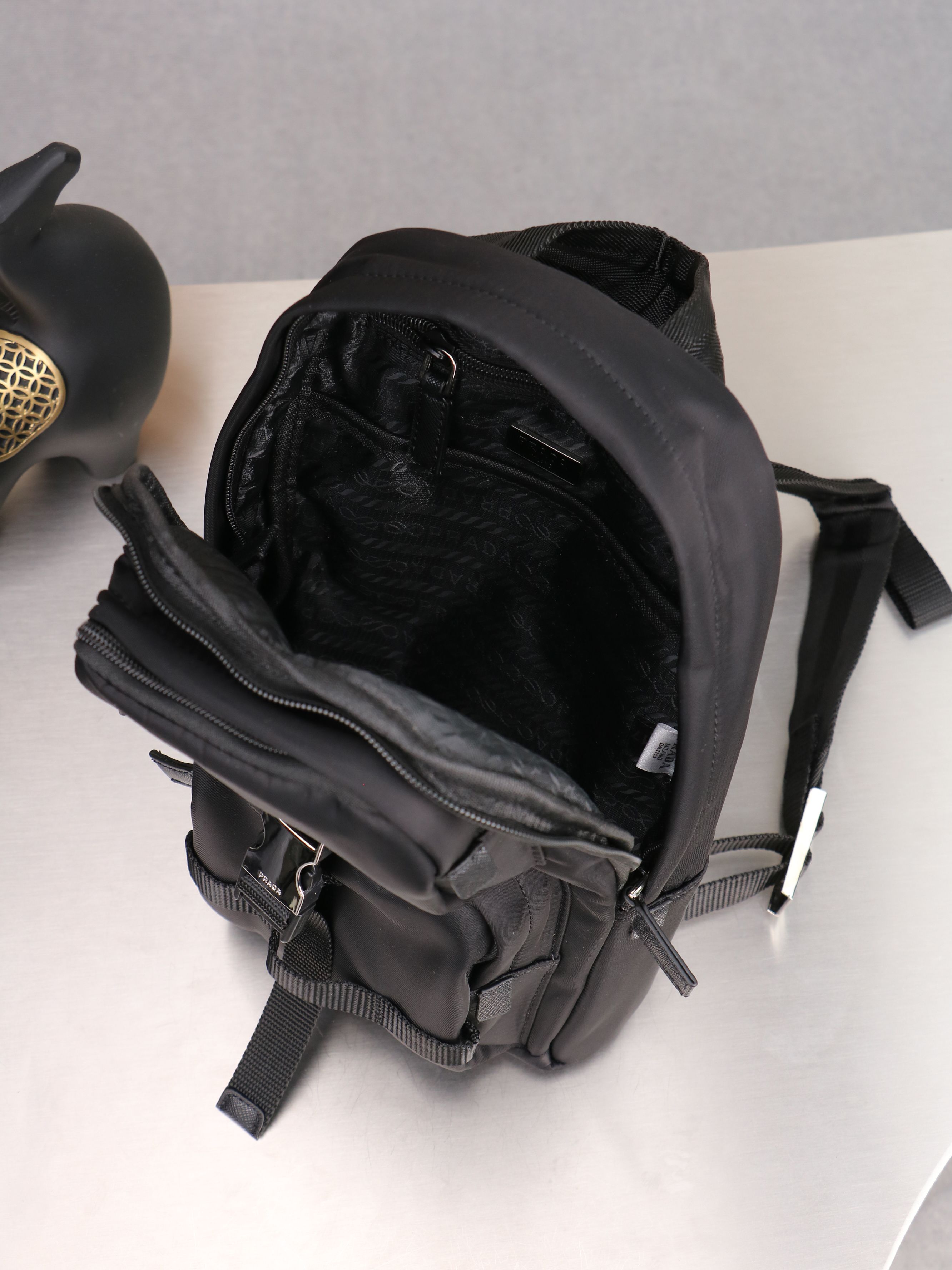 新款。P家专柜新款双肩吊袋🎒背包到货，ECONYL®再生尼龙和Saffiano皮革材质，再生尼龙涂胶织物贴饰+配带扣和磁