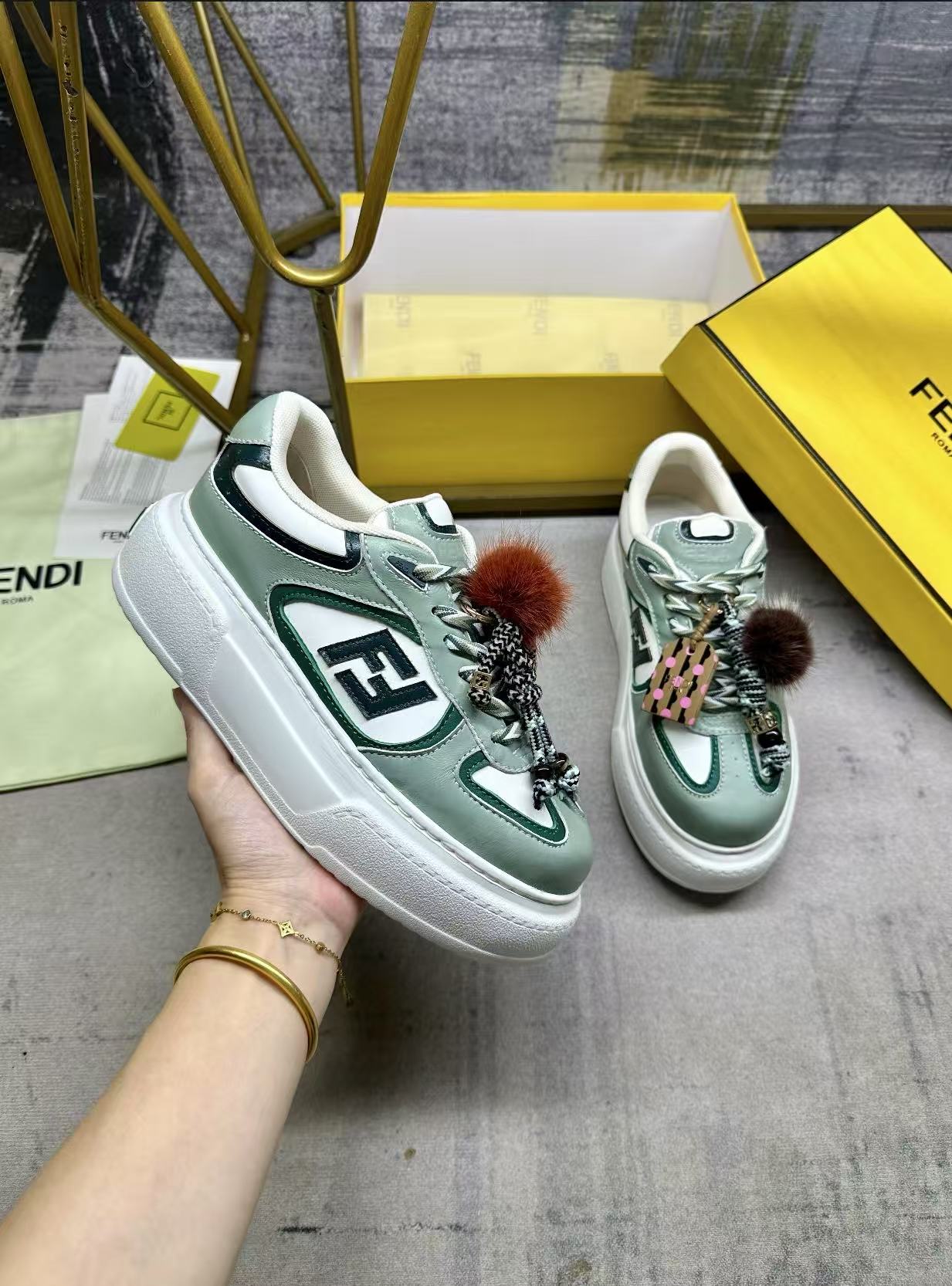 NO:592482,FENDI  Match lace-up sneakers. Light green fabric with green details. Contrast leather FF appliqués on the sides, white and green hiking laces. Thick rubber sole with oversized raised embossed FENDI lettering at the heel. Metal ring charm on the tongue. Contrast mink fur detailing and gold metal FF on the right shoe.  Small braided doll with graphic bracelet. The left shoe is decorated with a braided rope with contrasting mink double pom poms, metal FF beads and Pequin print pattern and logo (the doll is removable), sizes 35-42, casual shoes/sneakers, fendi, sneakers, bracelet19860909FENDI Match系带运动鞋.浅绿色面料,带绿色细节.侧边饰有撞色皮革FF贴花,白色和绿色登山鞋带.橡胶厚鞋底,后跟处饰有超大凸纹压花FENDI字样.鞋舌上饰有金属环挂饰右鞋上饰有带撞色貂毛细节和金色金属FF图案手链的编绳小玩偶.左鞋上饰有一条带撞色貂毛双绒球的编绳,饰有金属FF圆珠以及Pequin印花图案和标志（玩偶可拆卸）,35-42码,,休闲鞋/运动鞋,fendi,sneakers,bracelet,Women's Shoes