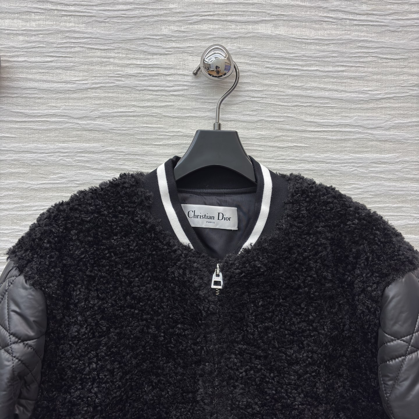 D家棒球夹克 是酷飒与温暖的完美融合 黑色毛绒主体柔软蓬松 菱格绗缝皮袖利落有型 经典黑白条纹饰边点缀细