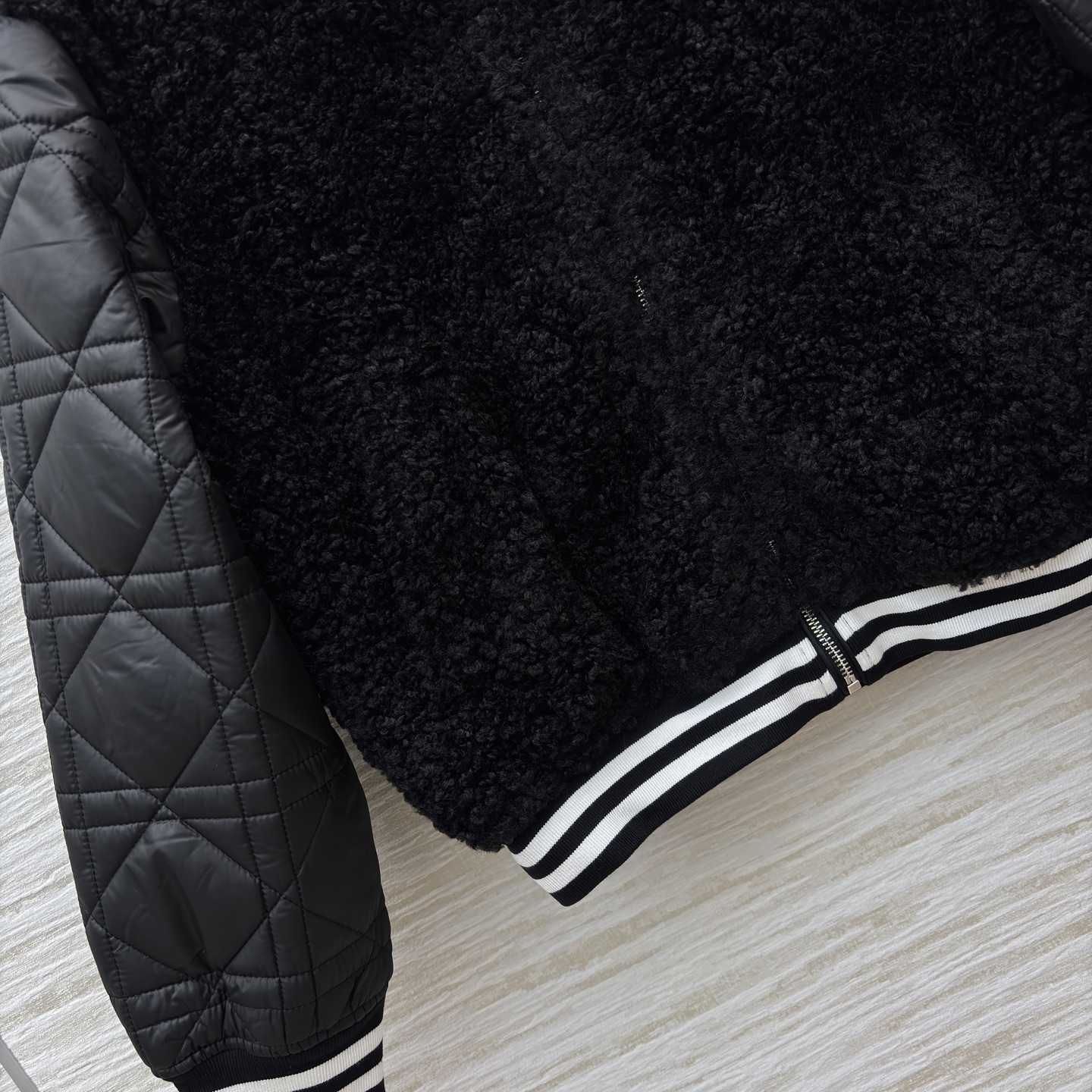 D家棒球夹克 是酷飒与温暖的完美融合 黑色毛绒主体柔软蓬松 菱格绗缝皮袖利落有型 经典黑白条纹饰边点缀细