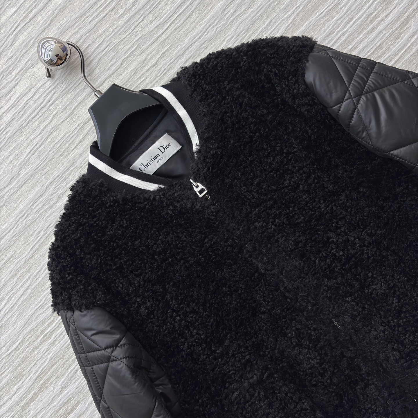 D家棒球夹克 是酷飒与温暖的完美融合 黑色毛绒主体柔软蓬松 菱格绗缝皮袖利落有型 经典黑白条纹饰边点缀细