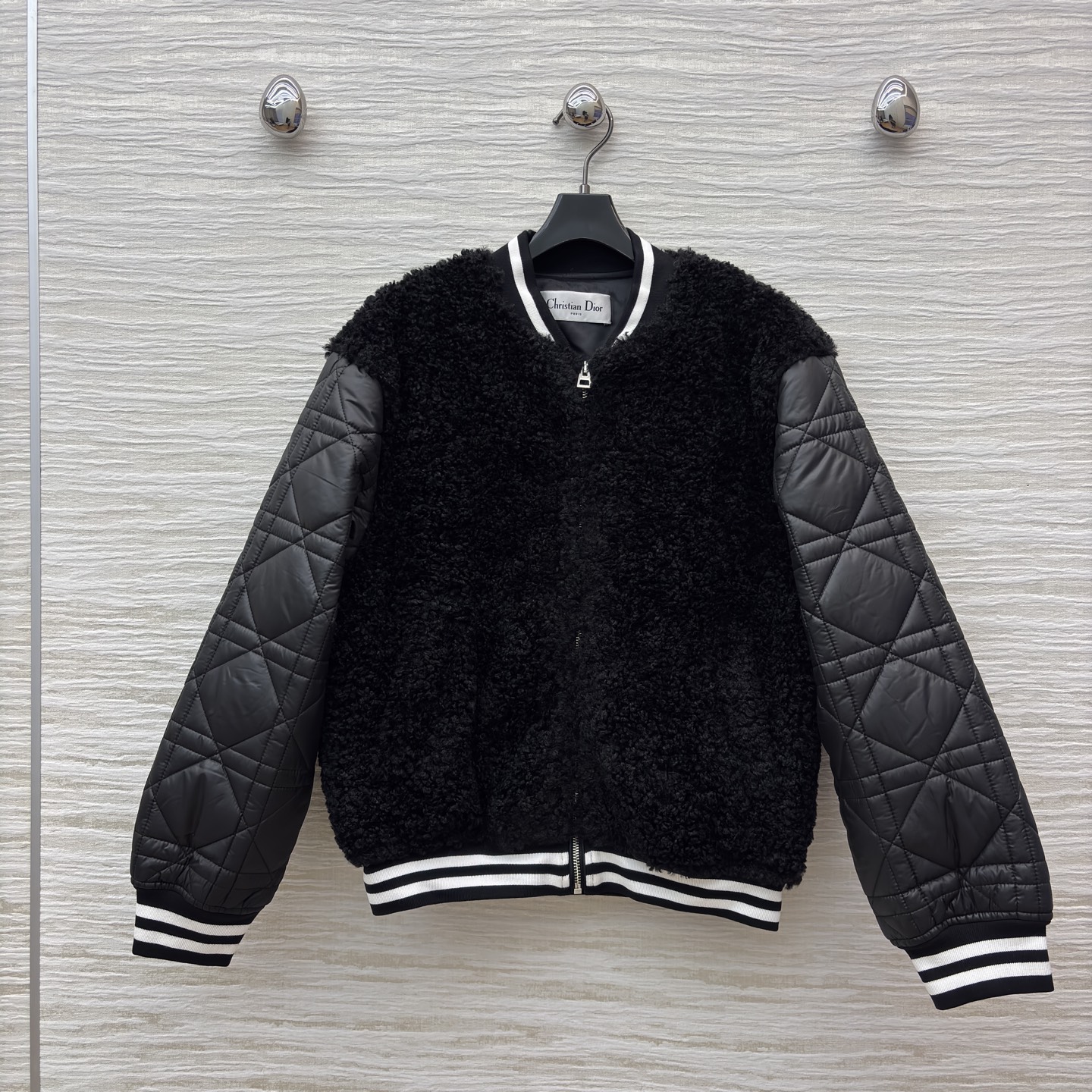 D家棒球夹克 是酷飒与温暖的完美融合 黑色毛绒主体柔软蓬松 菱格绗缝皮袖利落有型 经典黑白条纹饰边点缀细