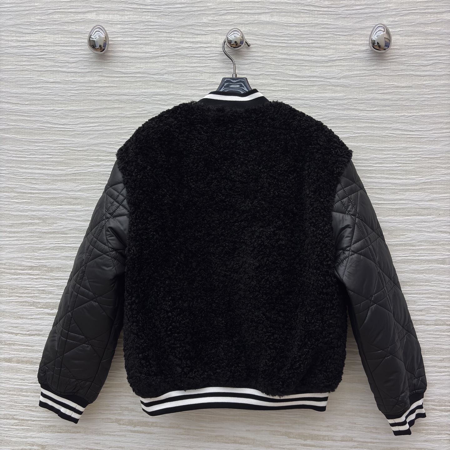 D家棒球夹克 是酷飒与温暖的完美融合 黑色毛绒主体柔软蓬松 菱格绗缝皮袖利落有型 经典黑白条纹饰边点缀细