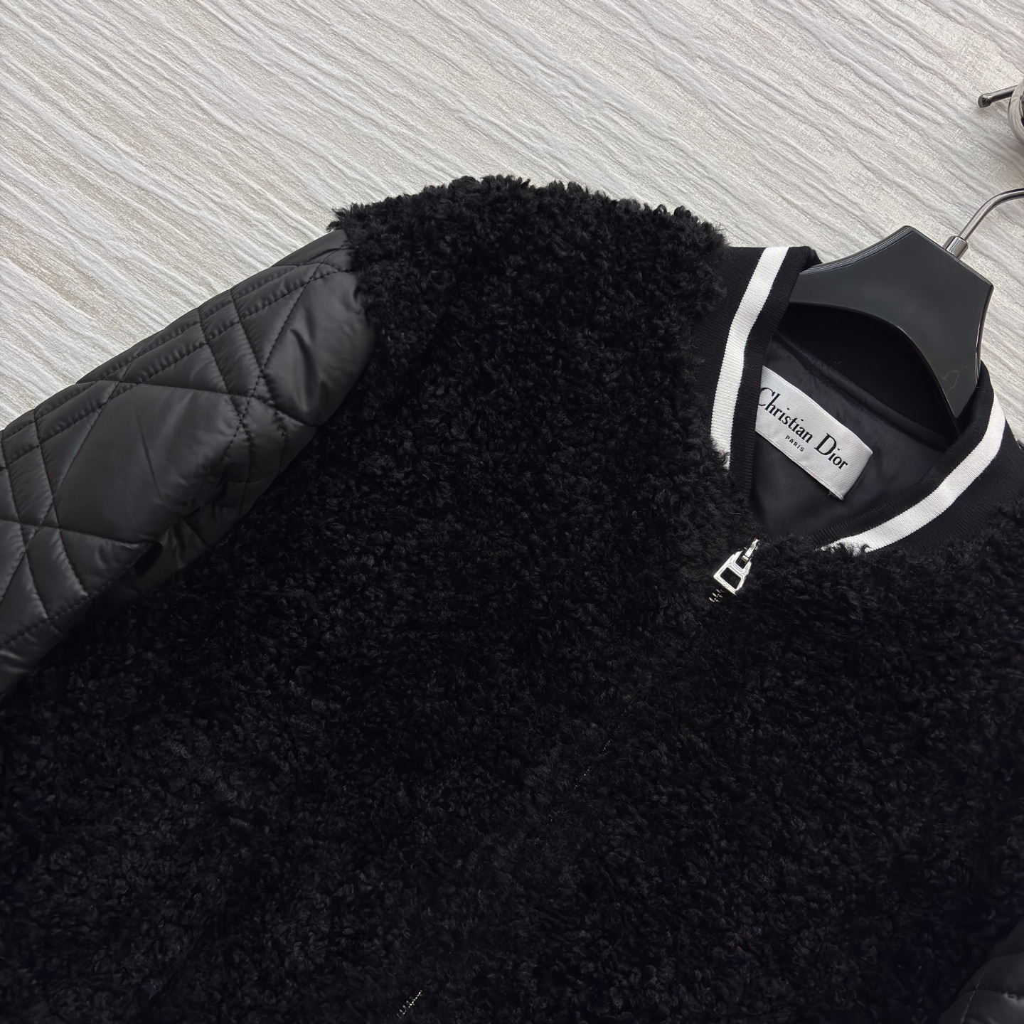 D家棒球夹克 是酷飒与温暖的完美融合 黑色毛绒主体柔软蓬松 菱格绗缝皮袖利落有型 经典黑白条纹饰边点缀细